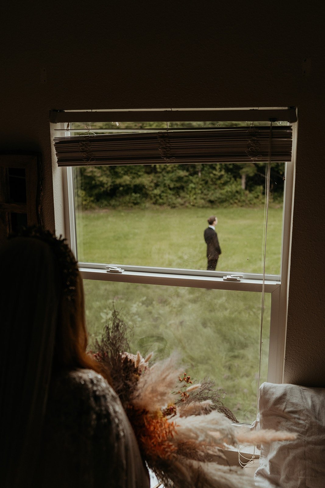 Bride looking out cabin window at groom waiting for their first look