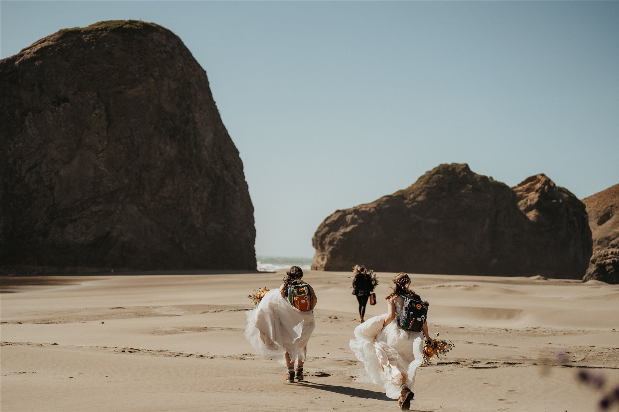 Brides walking across the beach in the wind for their elopement on the Oregon Coast