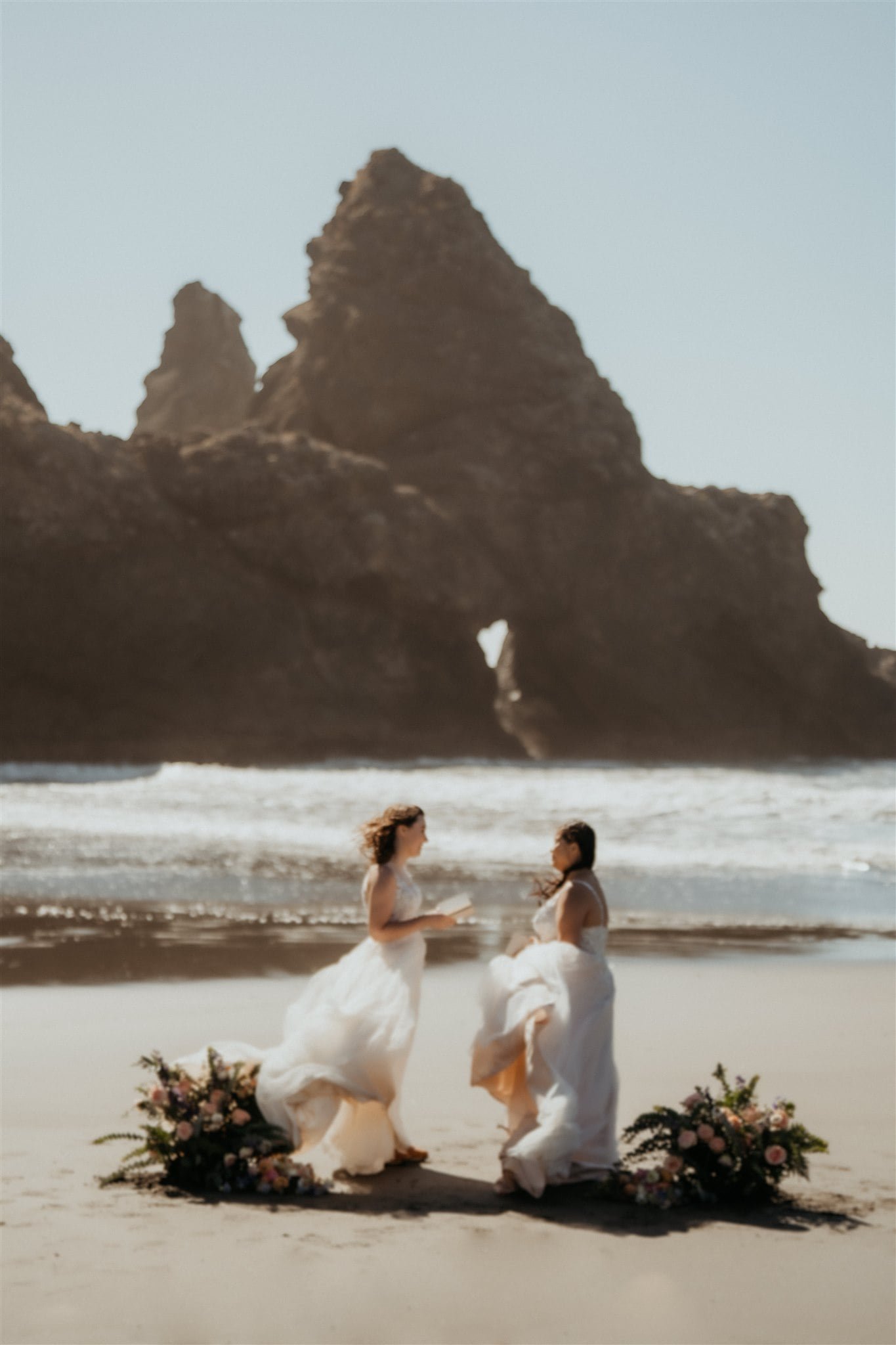 Brides exchange vows during their windy elopement ceremony on the beach on the Oregon Coast