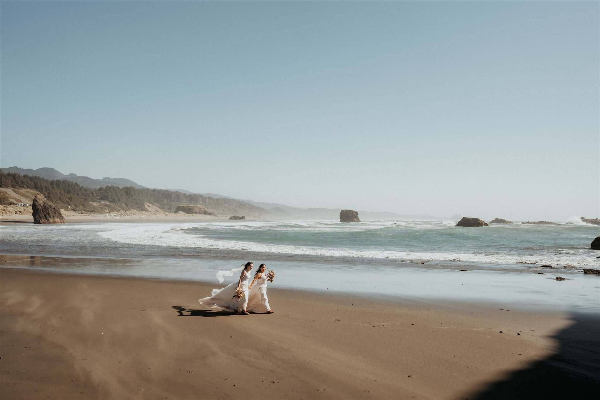 Brides walking in the wind across the beach on the Ore