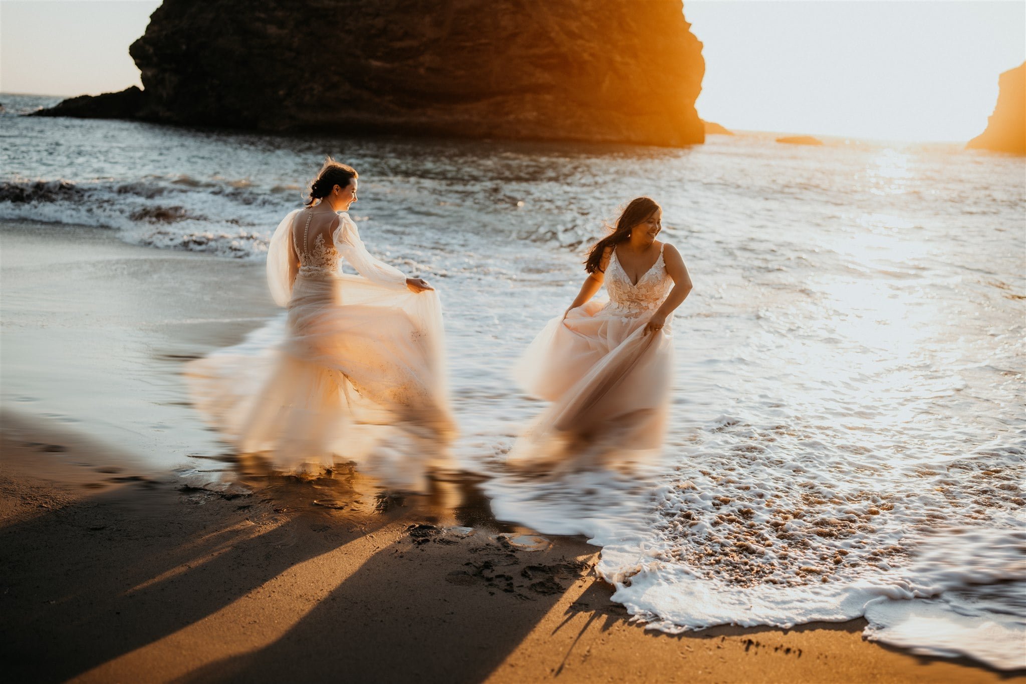 Brides splashing in the ocean during their sunset photos at Secret Beach, Oregon elopement