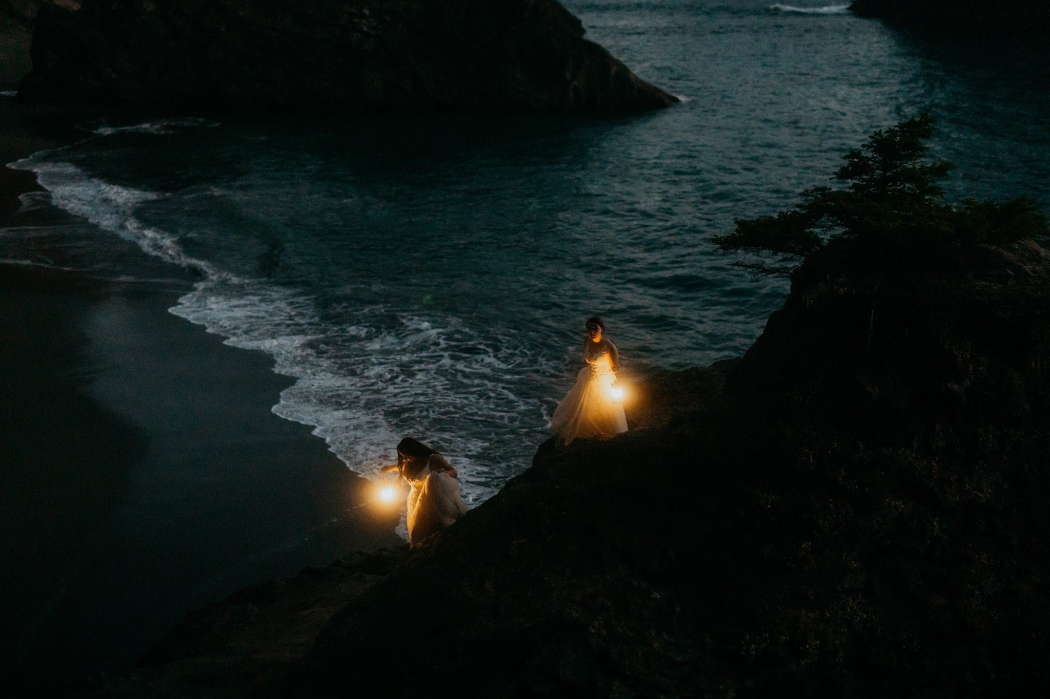 Two brides holding lanterns on the beach during blue hour portraits at elopement at Sunset Beach, Oregon