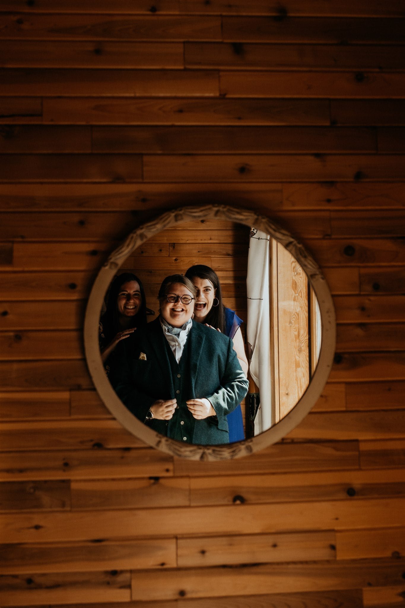 Bride looking at herself in the mirror while friends look on excitedly 