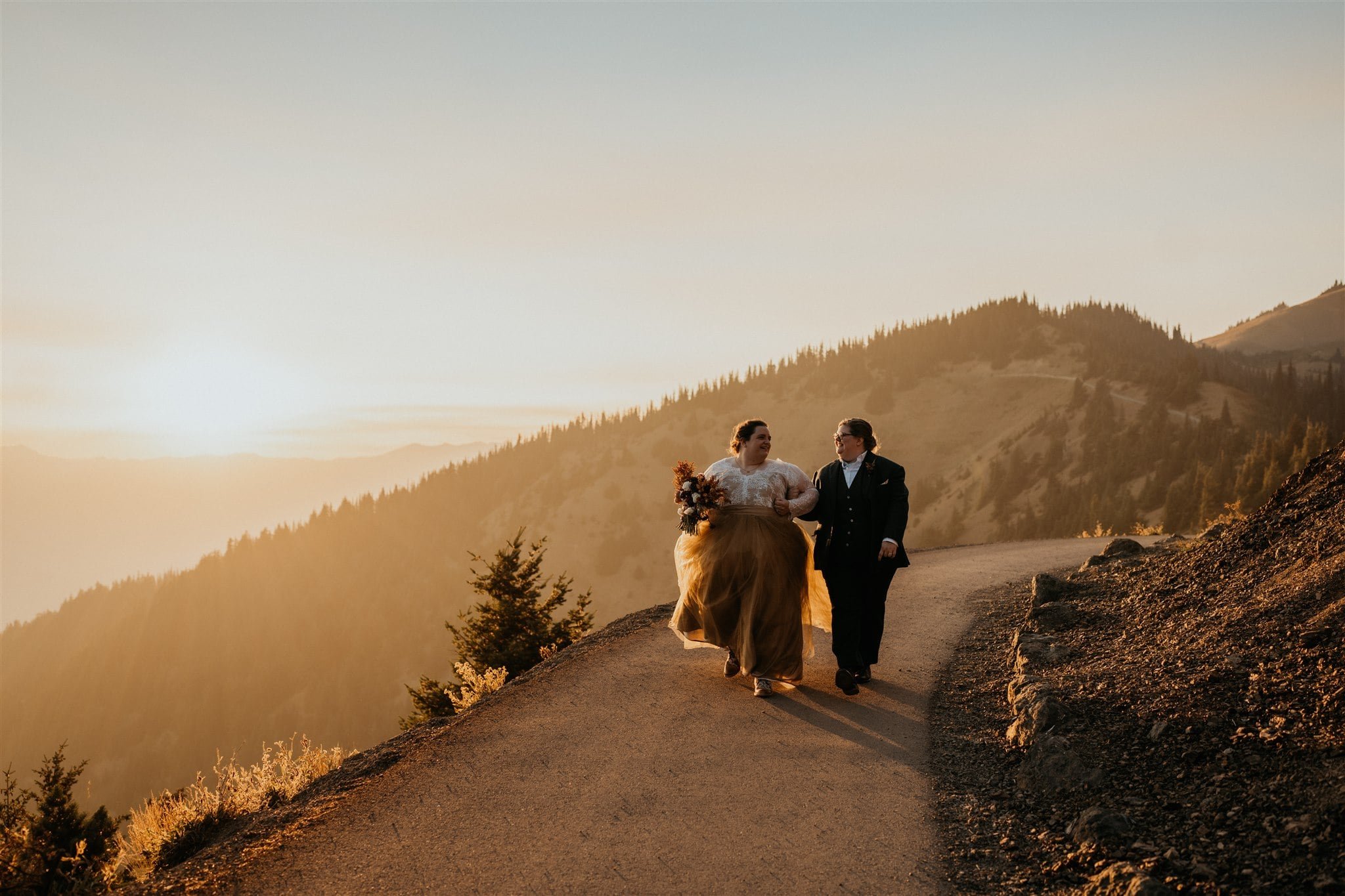 Brides hold hands while walking down a trail at Olympic National Park elopement