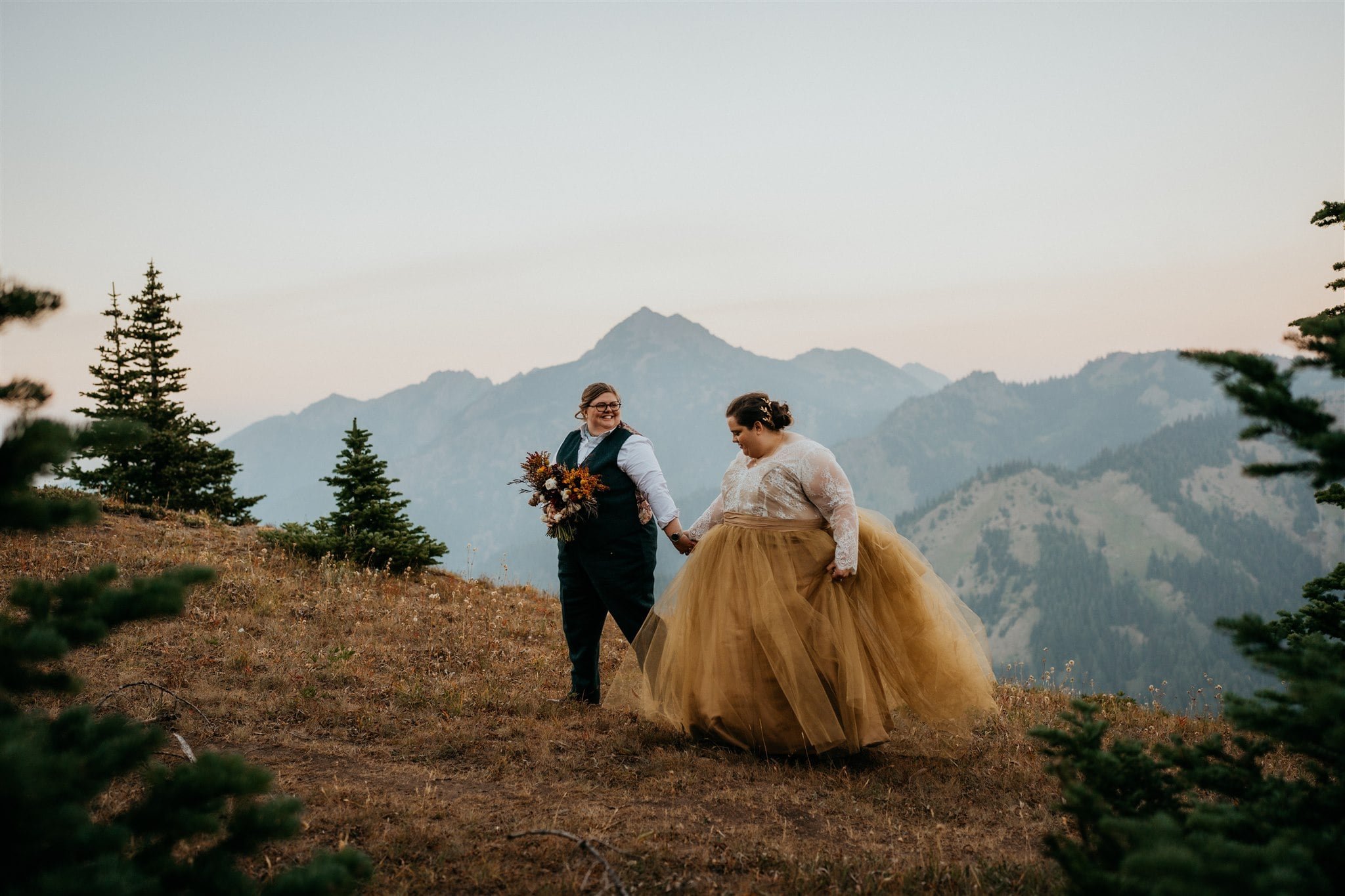 Brides walk through a meadow at sunset during their Lake Crescent elopement