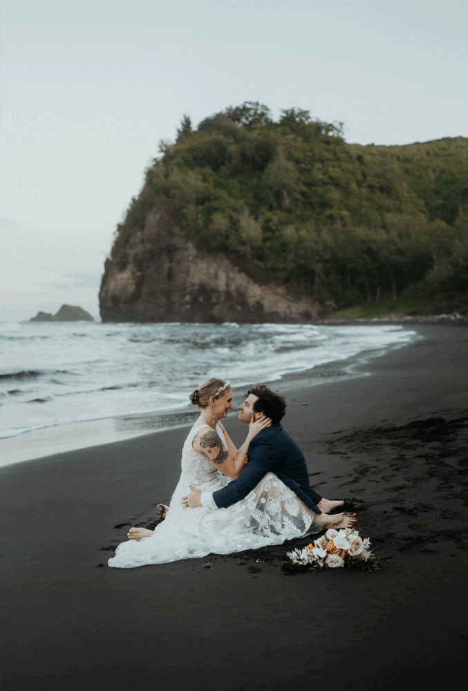 Bride and groom sit and kiss on the black sand beach during their Big Island elopement