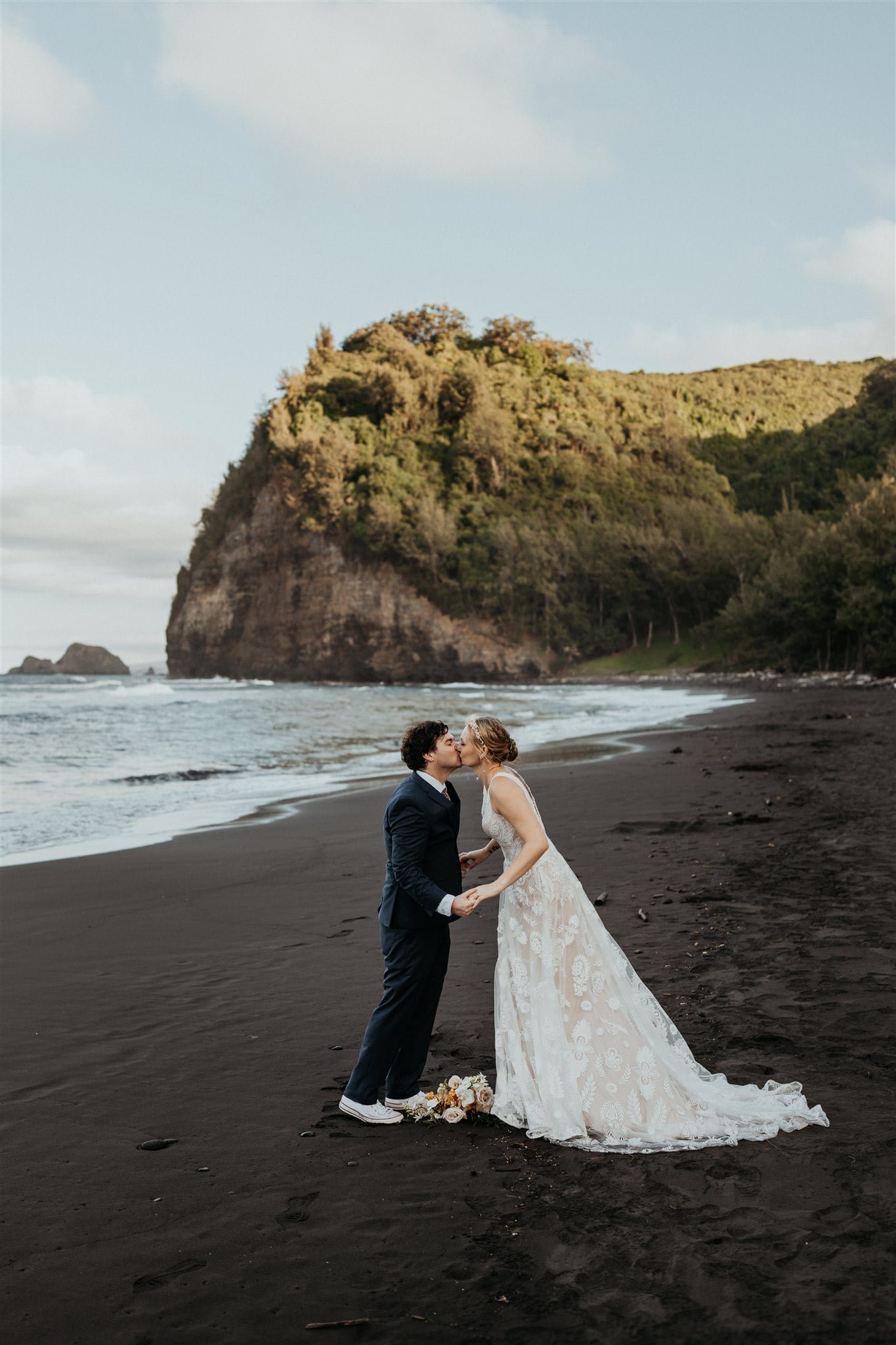 Bride and groom kiss after their elopement ceremony on a black sand beach on the Big Island