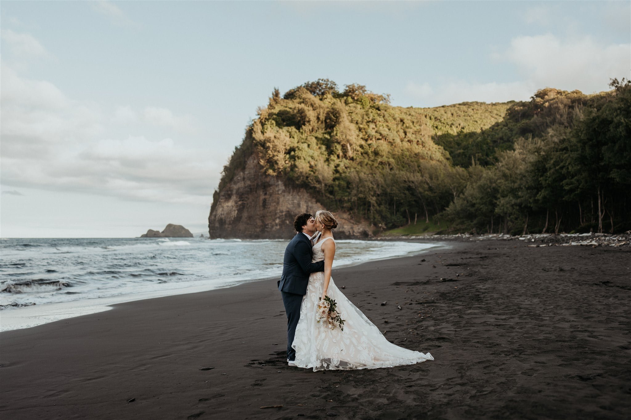 Bride and groom kiss after their elopement ceremony on a black sand beach on the Big Island