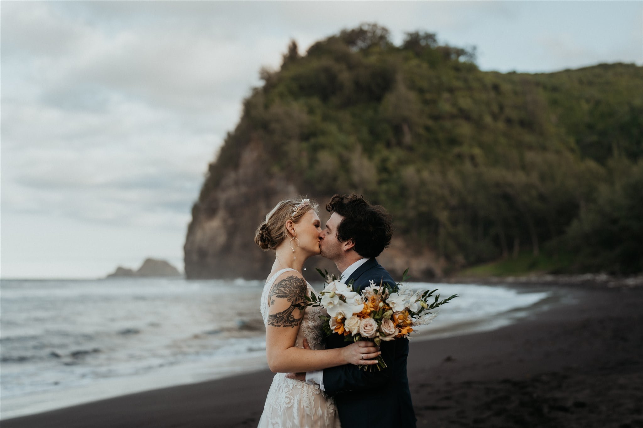 Bride and groom kiss on the black sand beach during their elopement in Hawaii