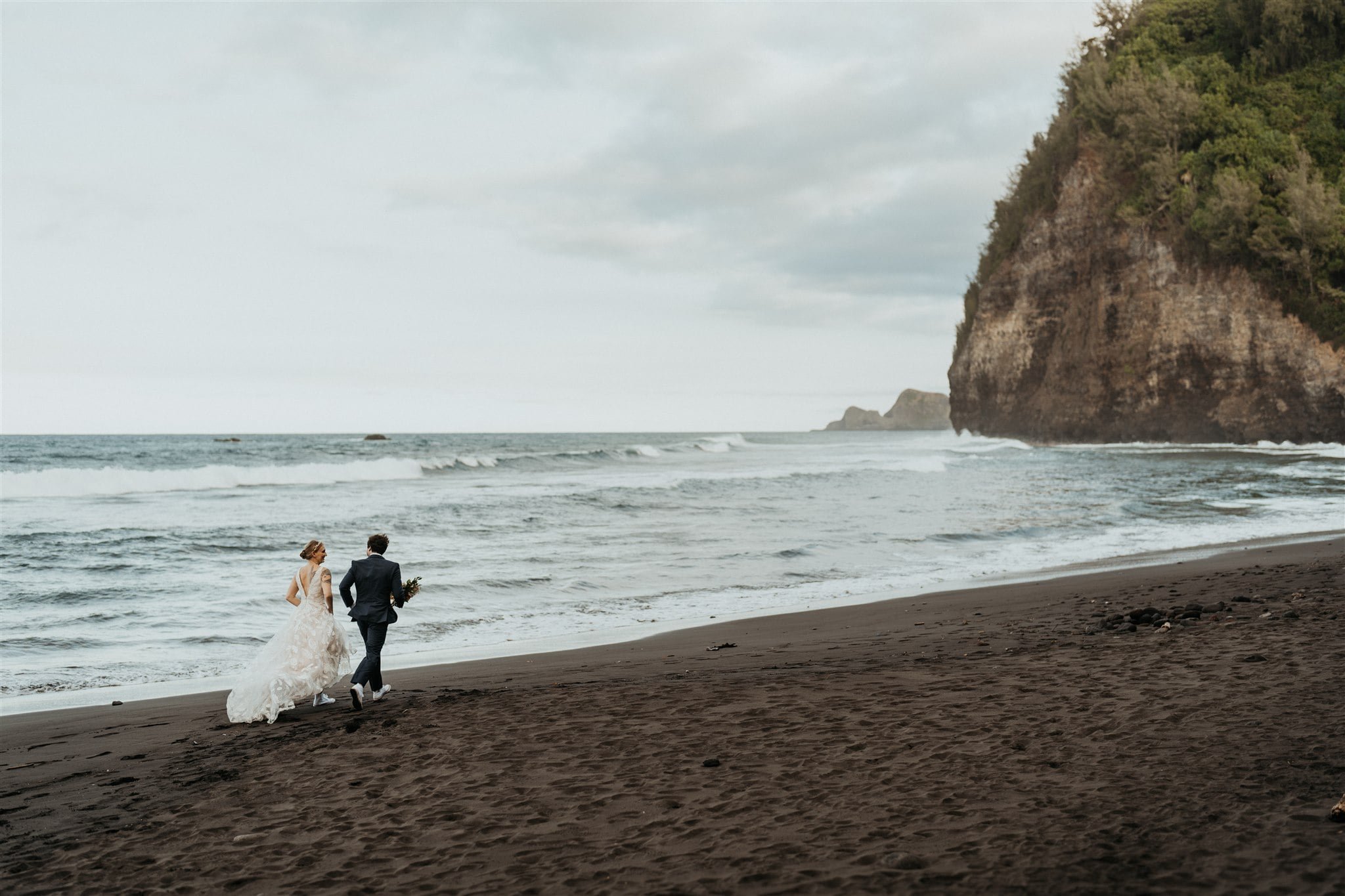 Bride and groom run across the black sand beach while they elope on the Big Island