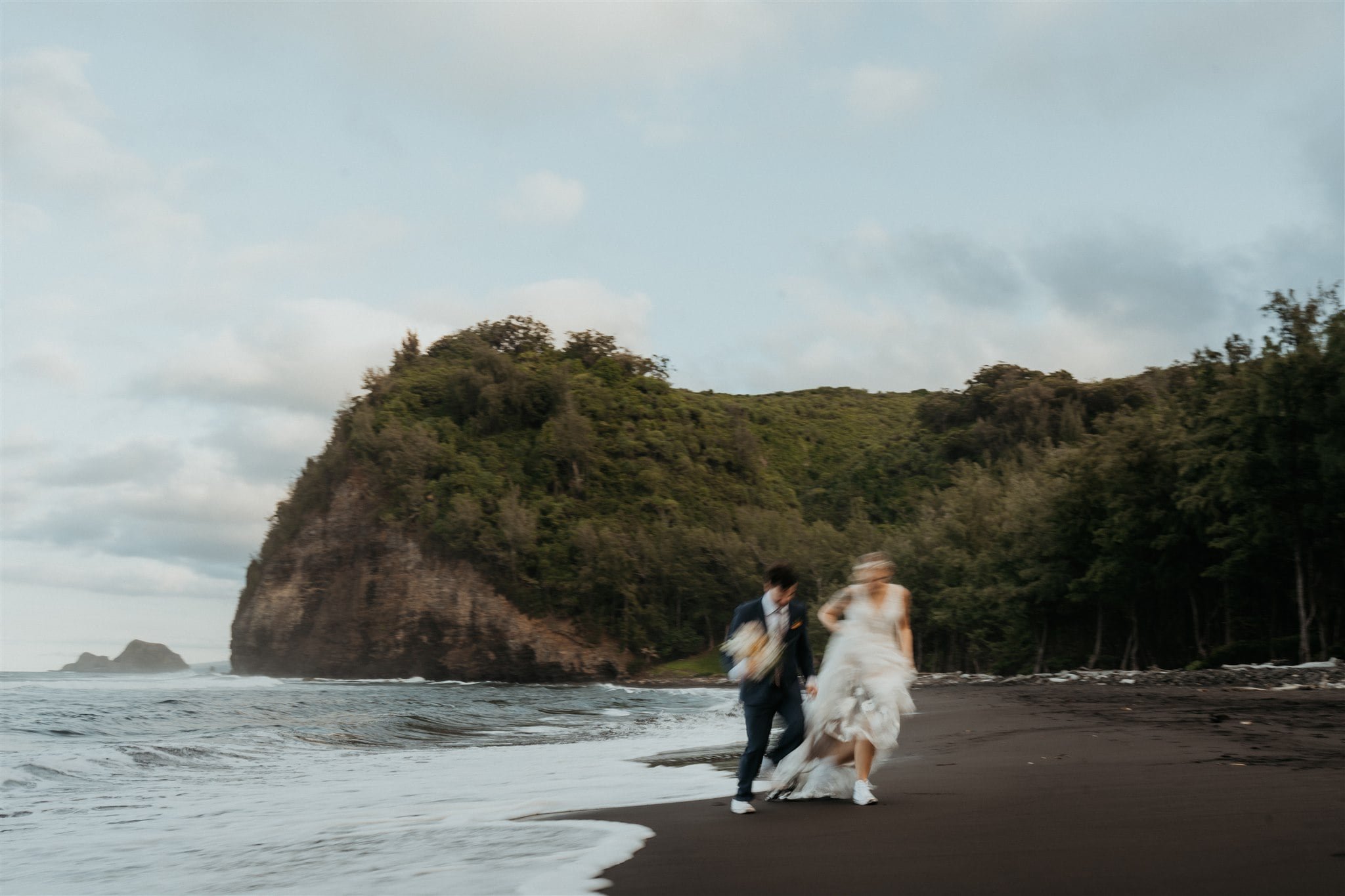 Bride and groom hold hands while running across the beach at their Big Island elopement