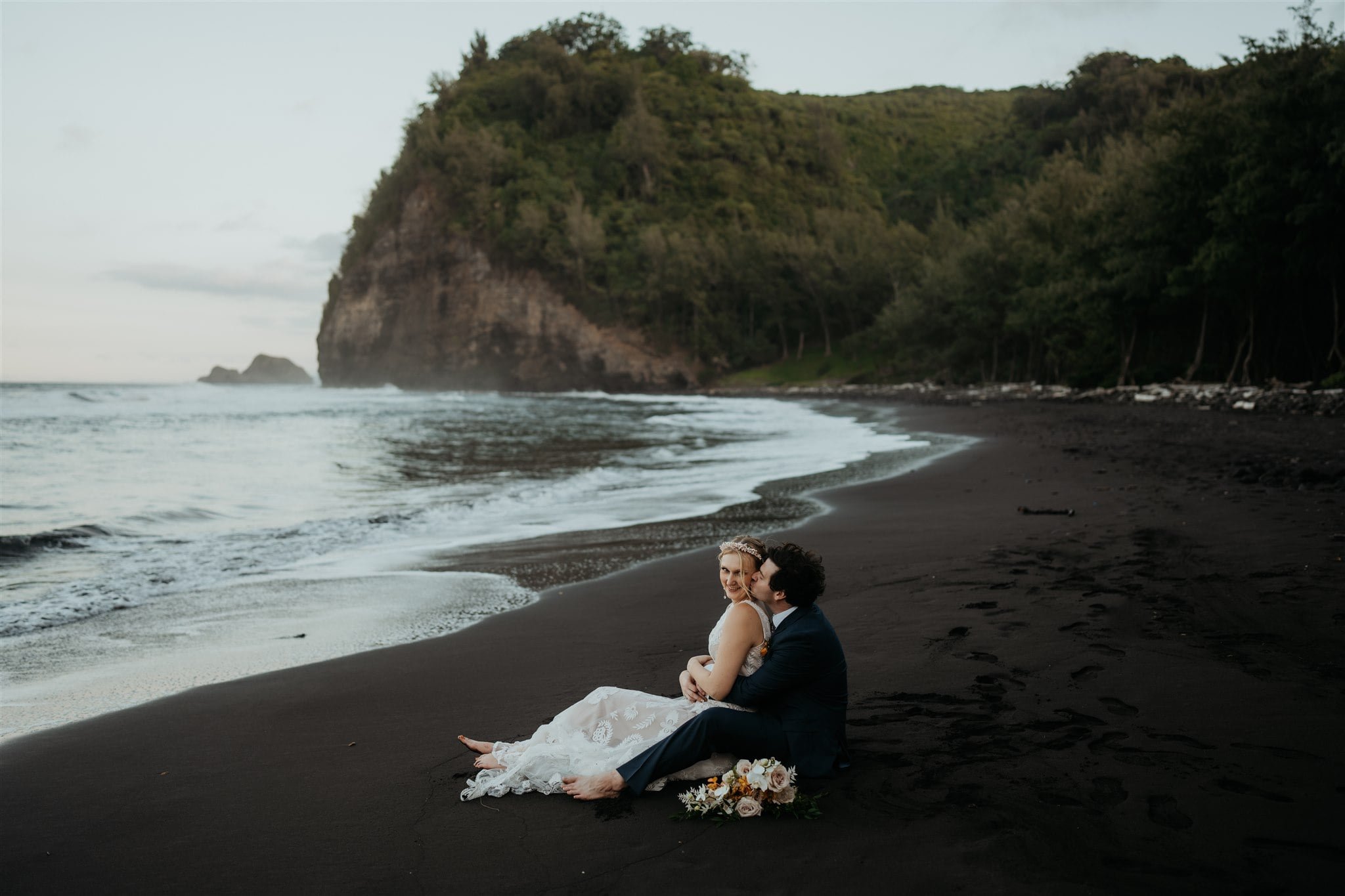Bride and groom sit on the black sand beach during their Big Island elopement