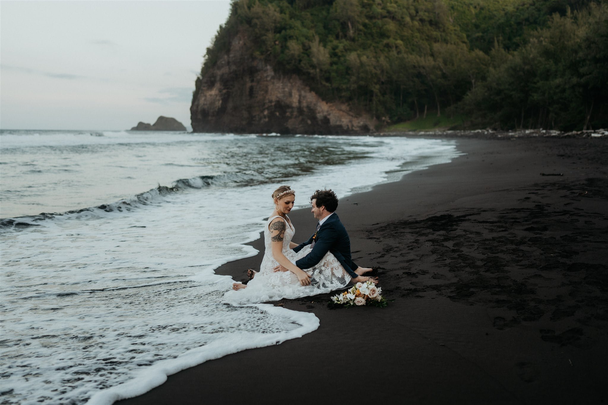 Bride and groom sit on the black sand beach for their Hawaii elopement photos