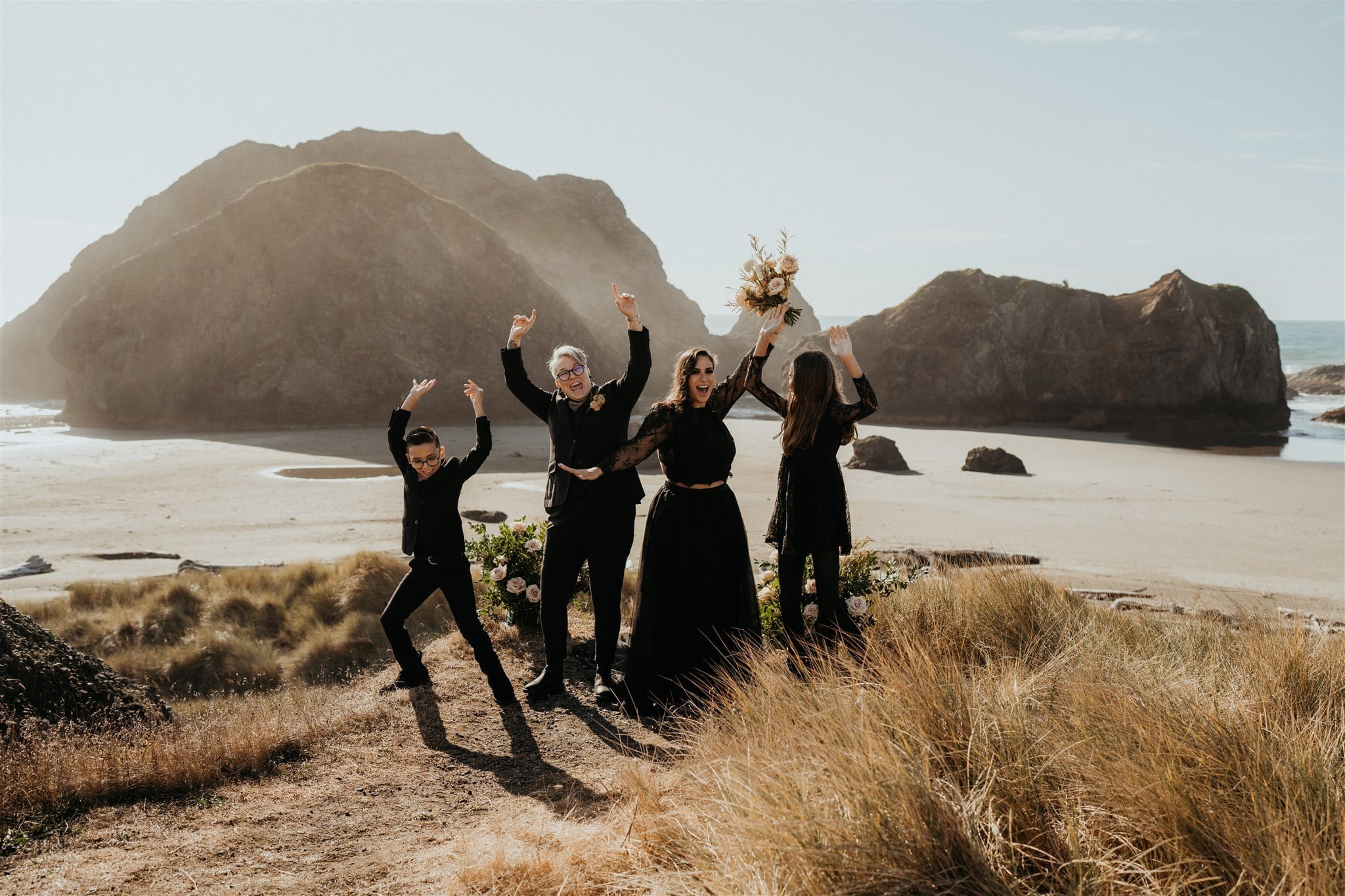Brides and children in all black wedding attire cheer after Oregon Coast elopement ceremony