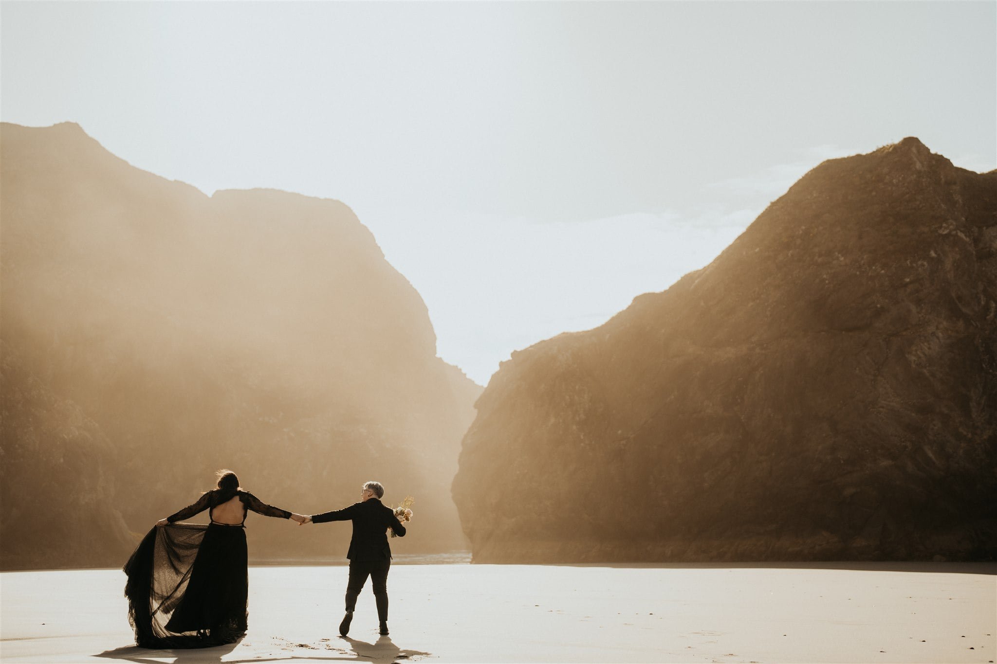 Two brides hold hands and walk across the beach during their Pacific Northwest elopement