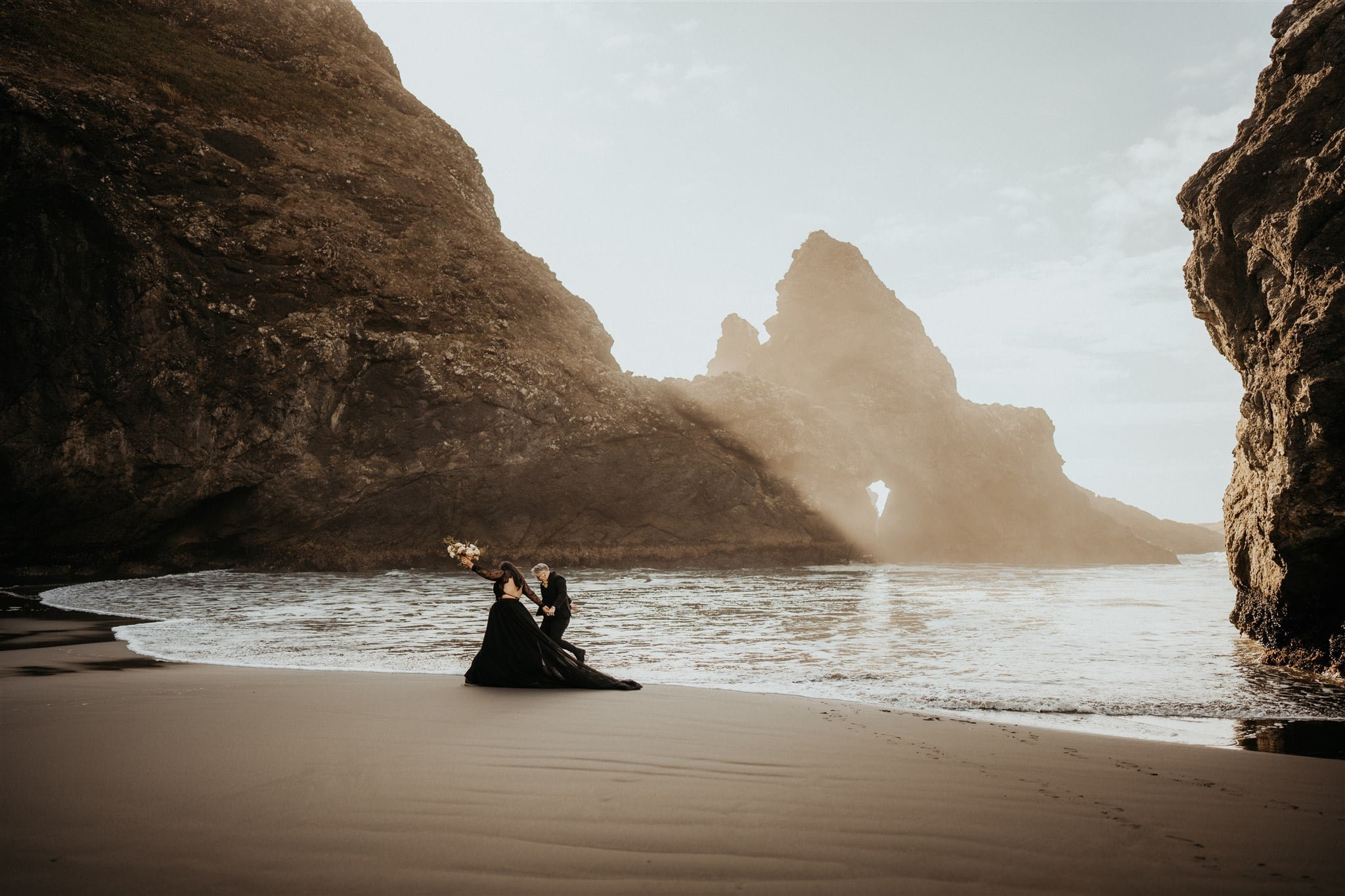 Brides walk across the beach on the Oregon Coast during sunset 