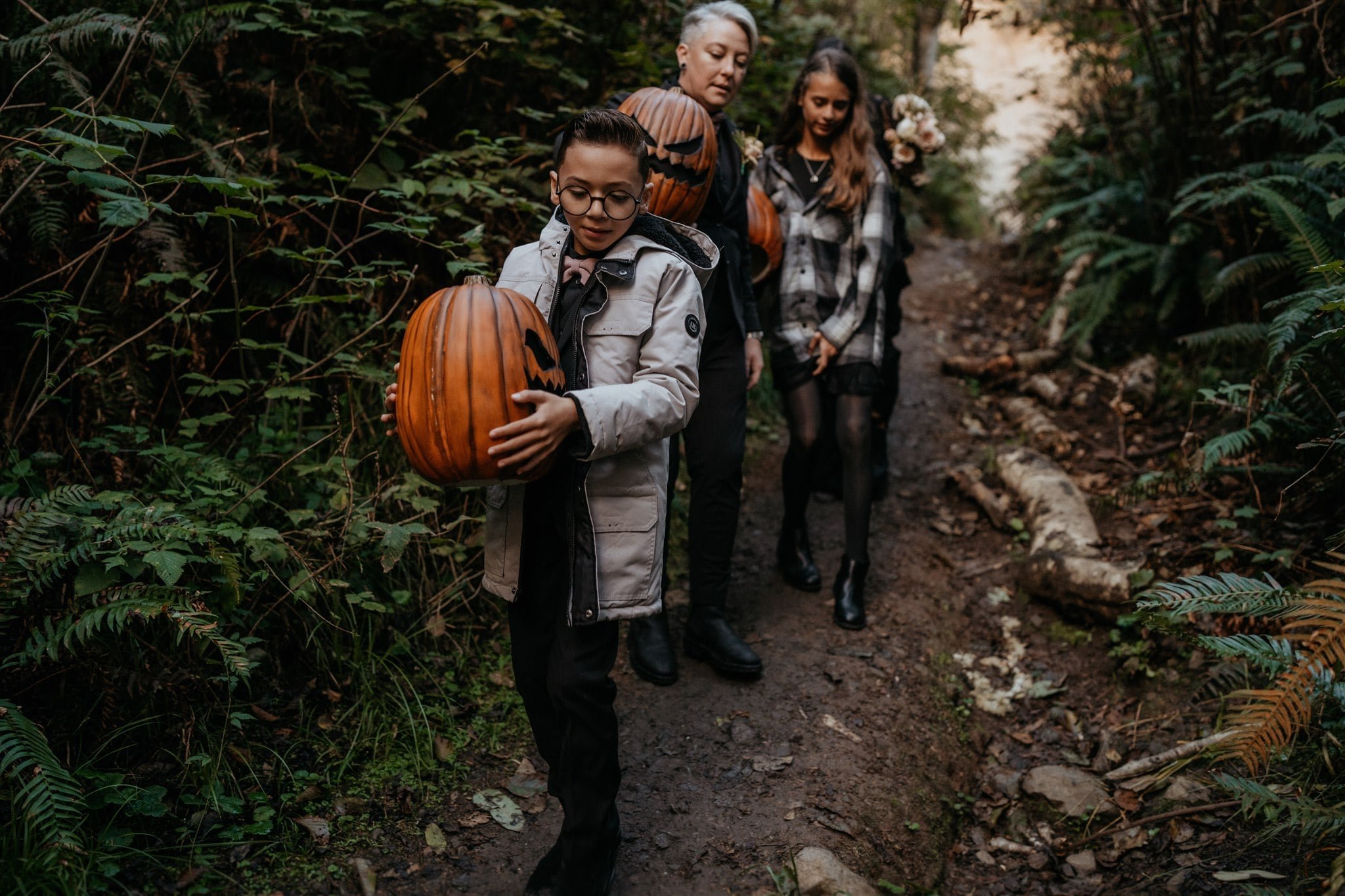 Brides and kids carry pumpkins on a hiking trail in the Pacific Northwest