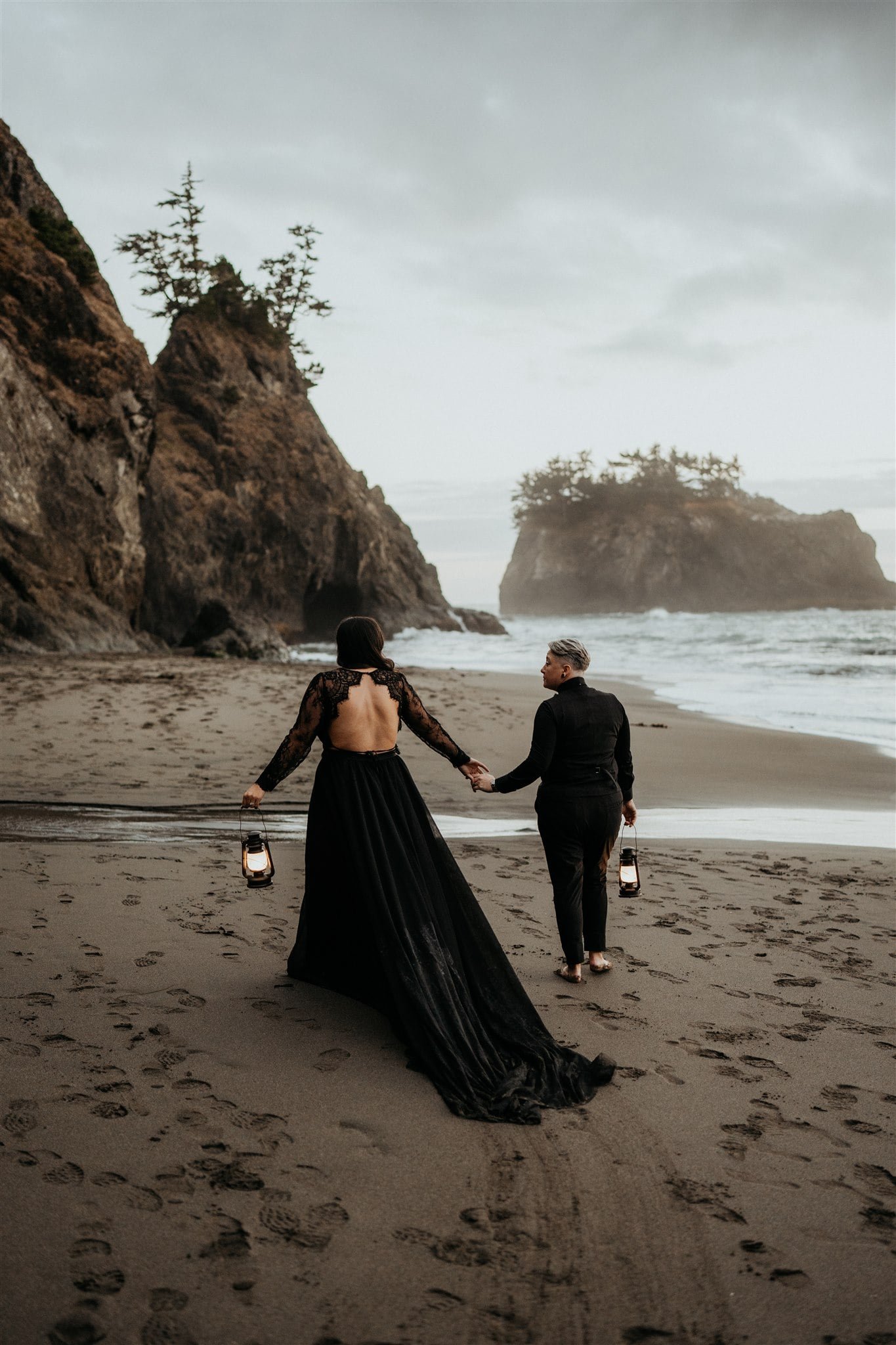 Two brides walk across the beach holding lanterns during their Oregon Coast elopement