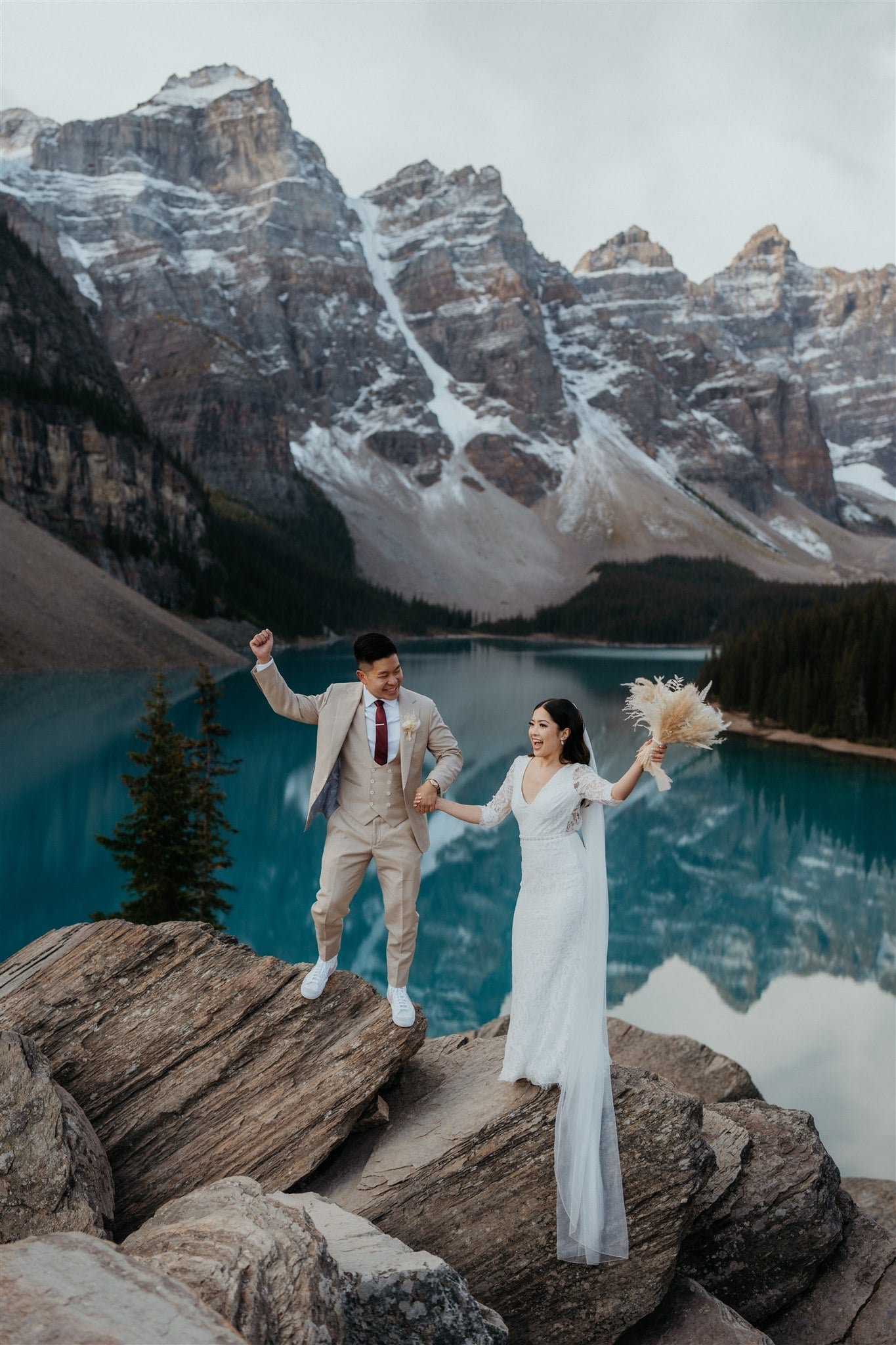 Bride and groom hold hands on a rock during their sunrise elopement photos at Banff National Park