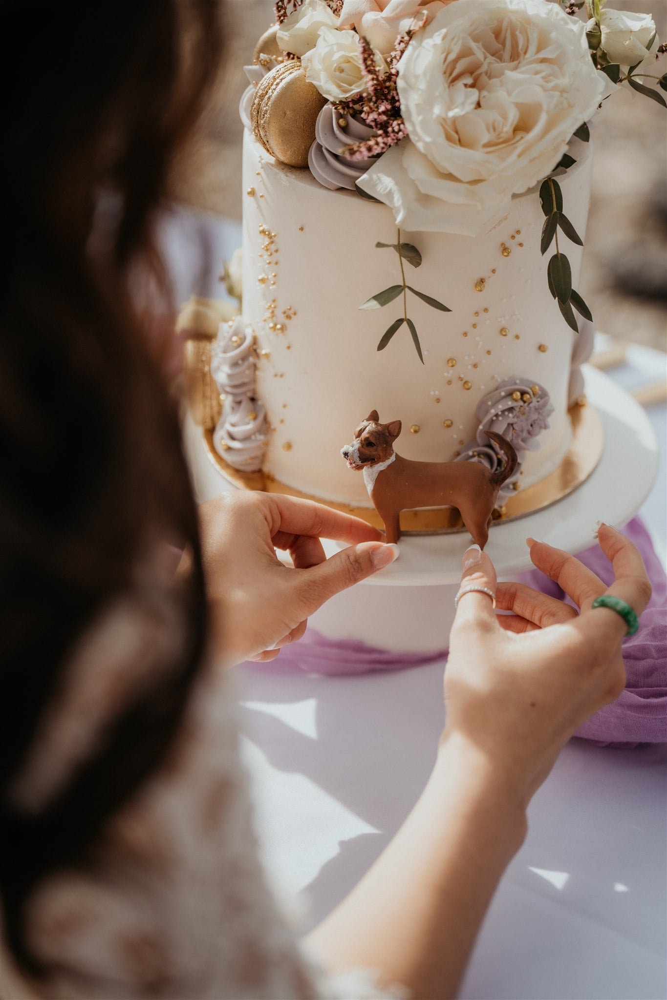 Bride cuts a slice of white wedding cake decorated with dried florals