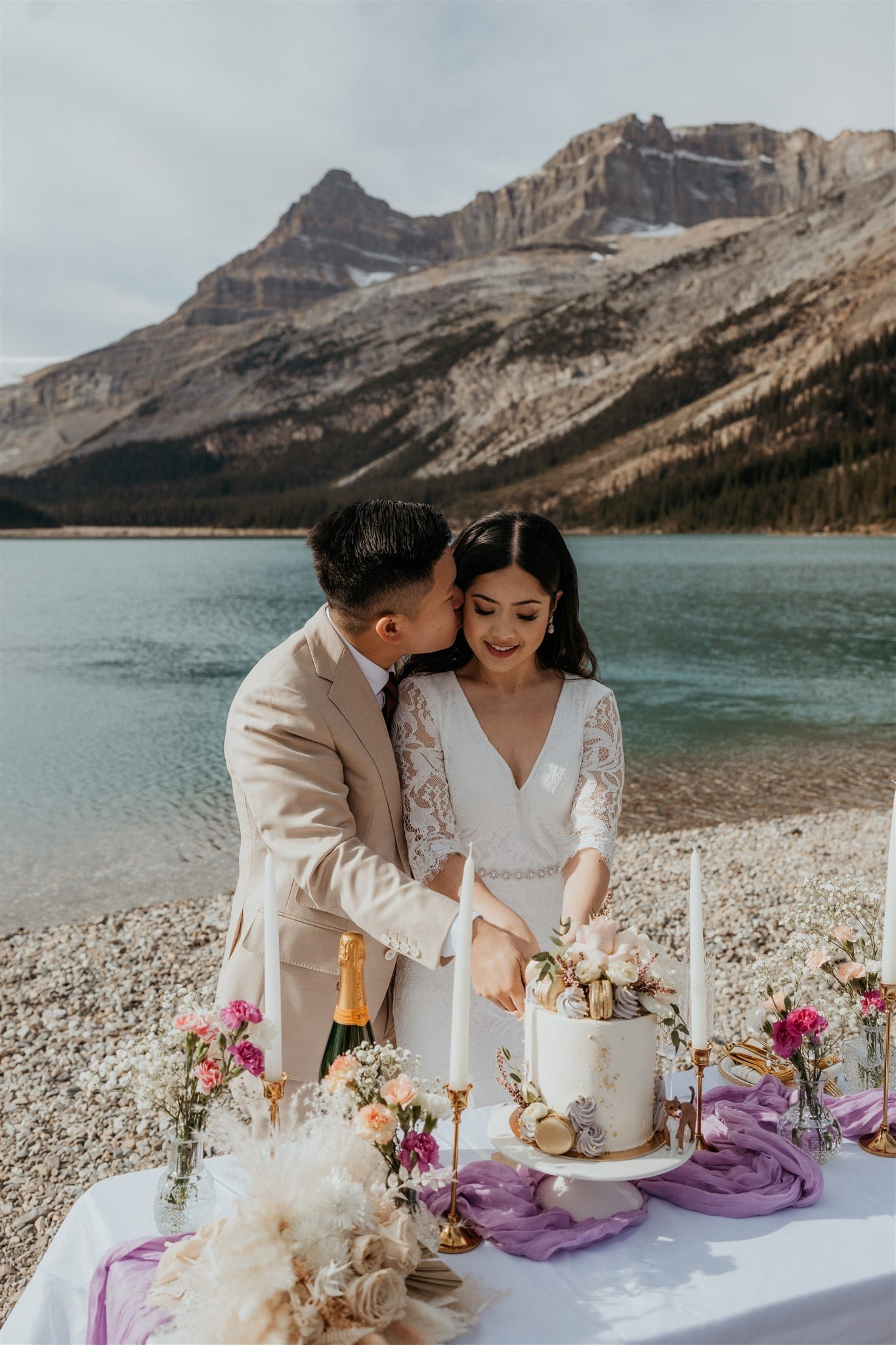 Groom kisses bride on the cheek while they cut their wedding cake in Banff National Park