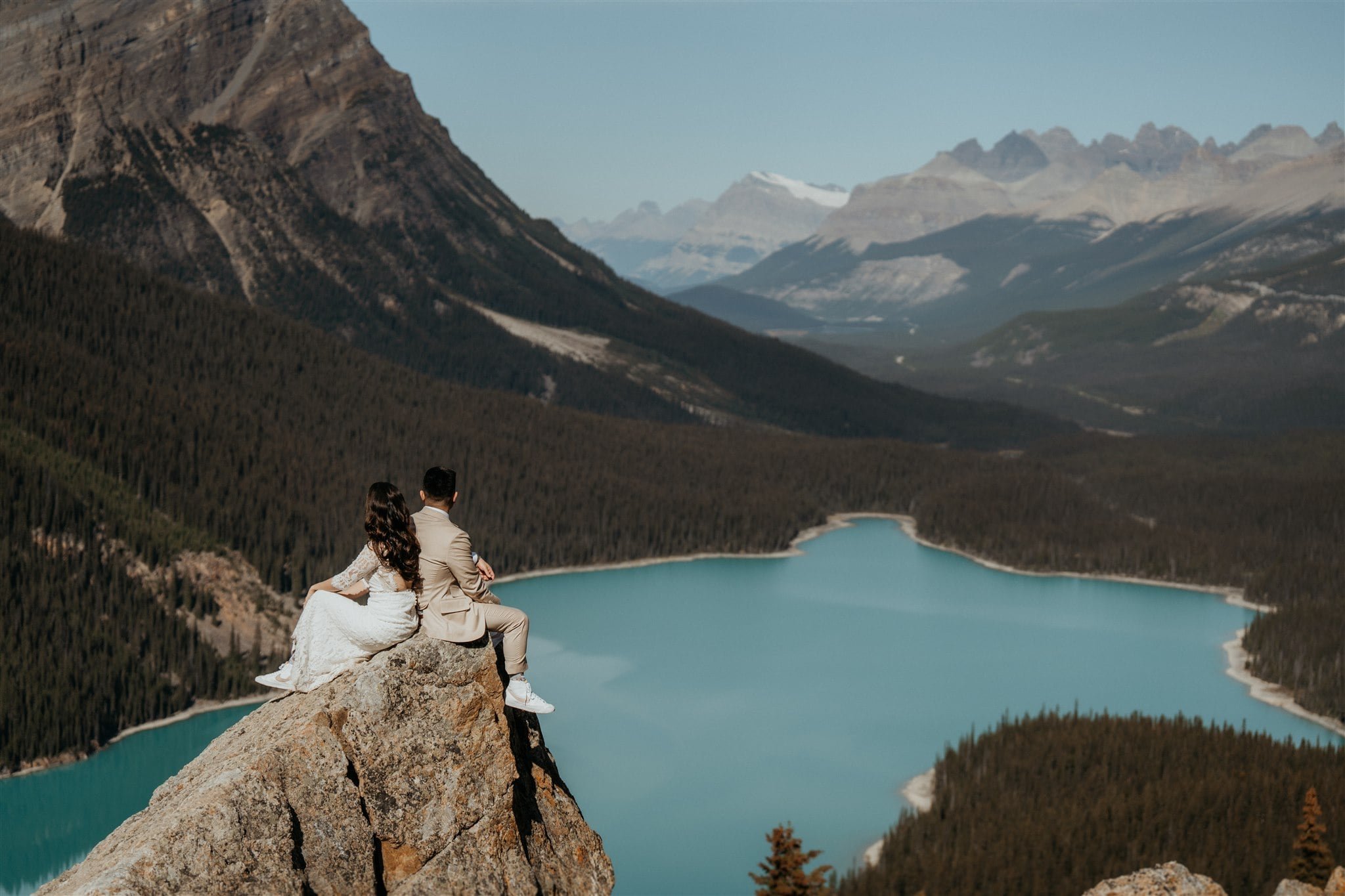 Bride and groom sit on top of a rock looking out over a lake at their Banff National Park elopement