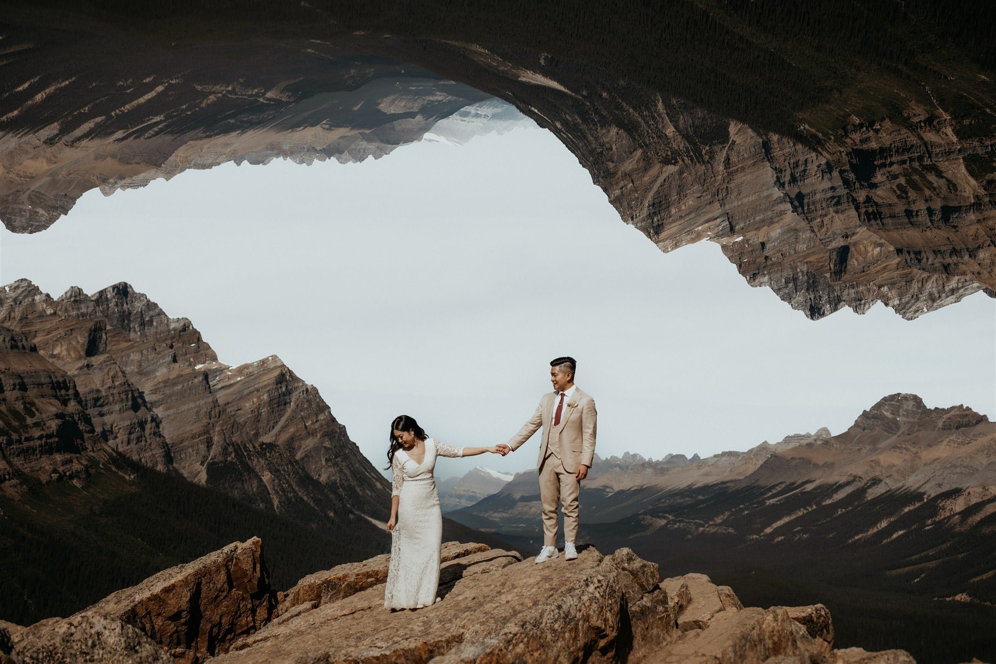 Bride and groom hold hands on top of a mountain at their elopement in Banff National Park