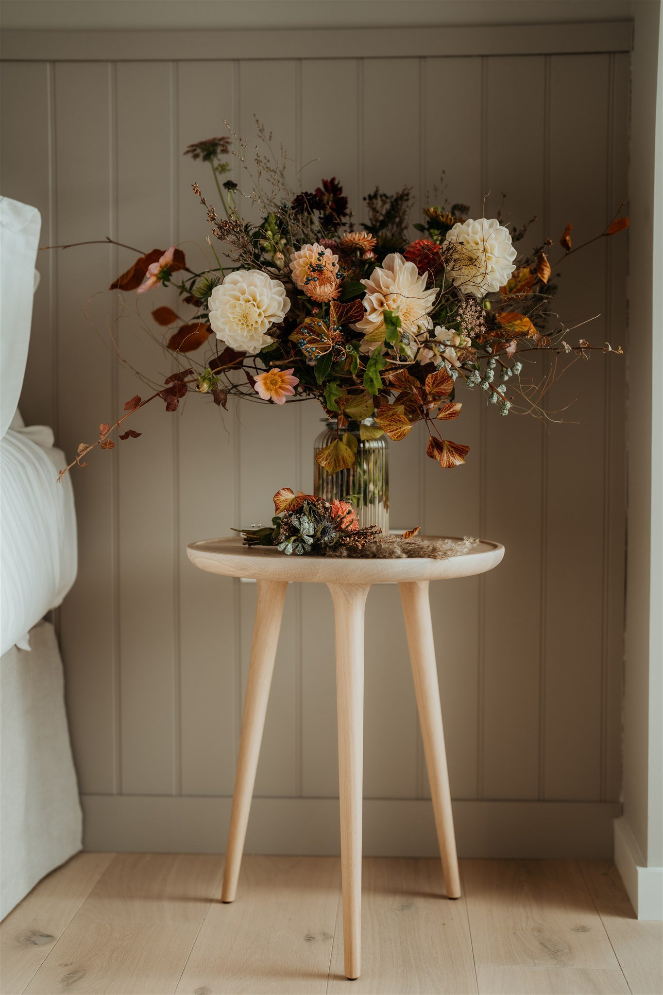 Orange, cream, and brown wedding flowers sitting in a vase on a bedside table 