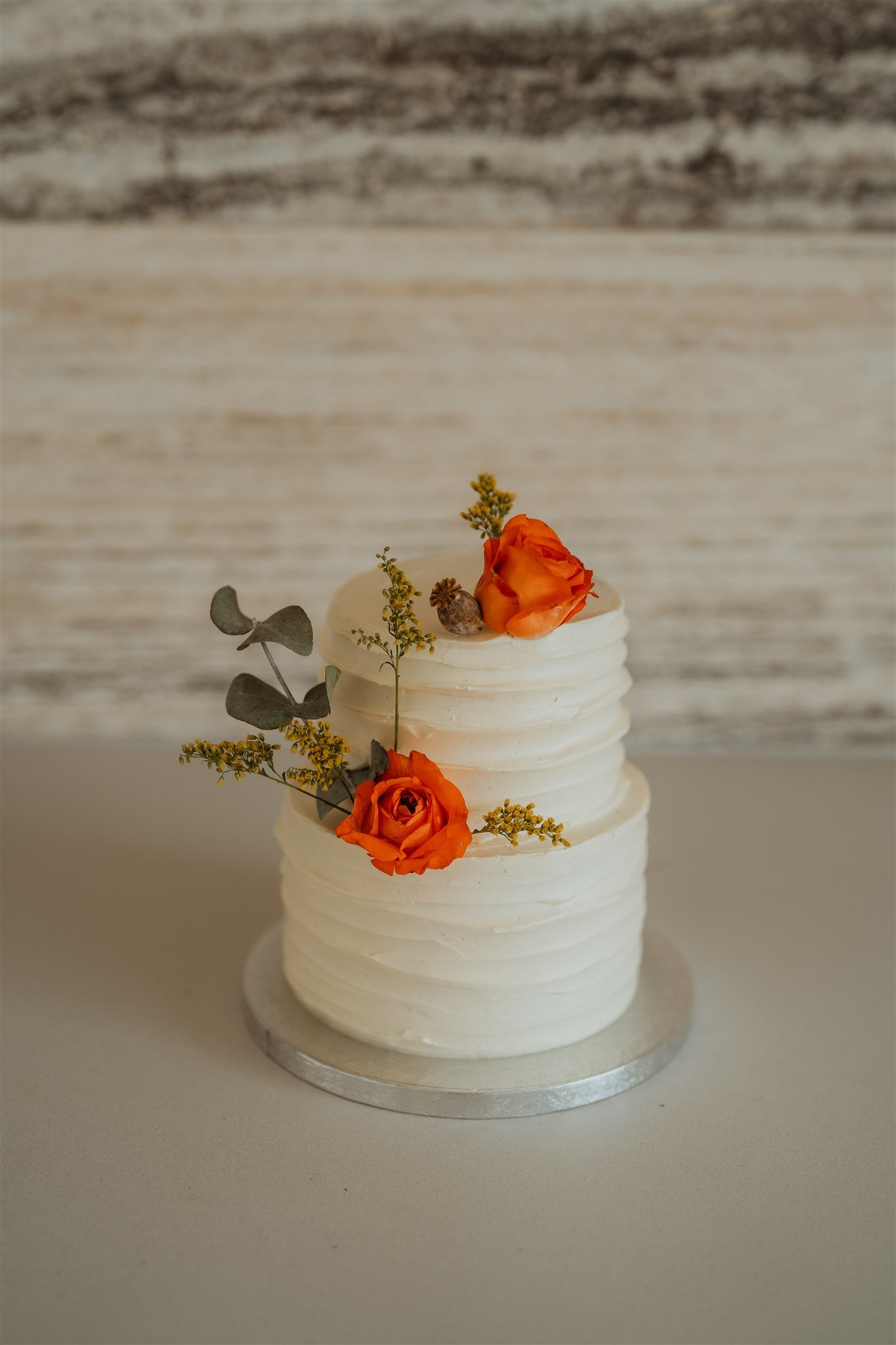 White two layer frosted wedding cake with orange flowers
