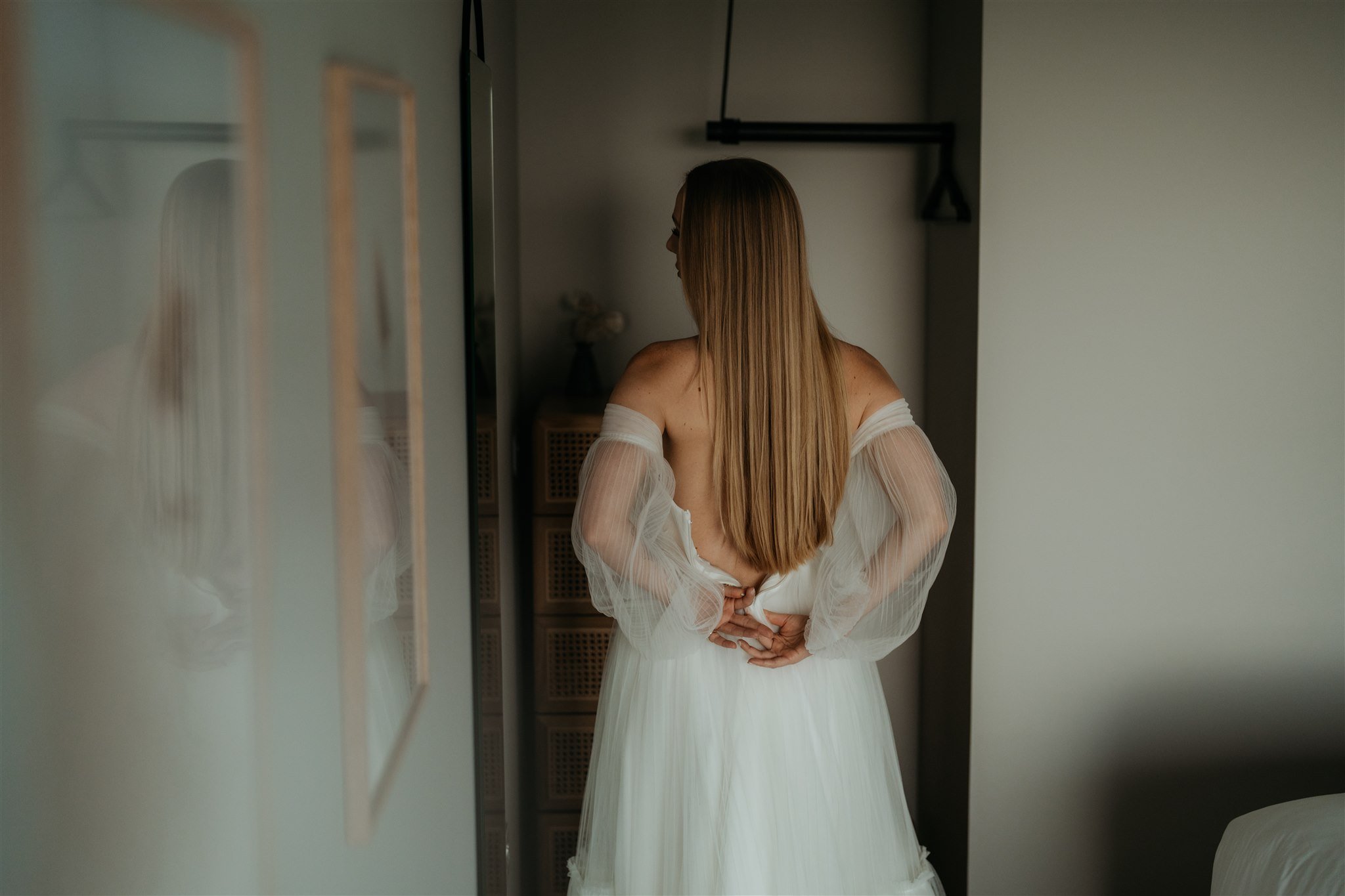 Bride zipping up the back of her white wedding dress while getting ready for her Isle of Skye elopement