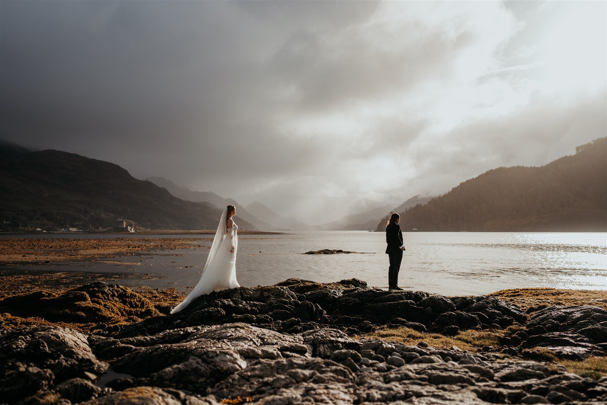 Brides stand on a rock by the water getting ready for their elopement first look on the Isle of Skye