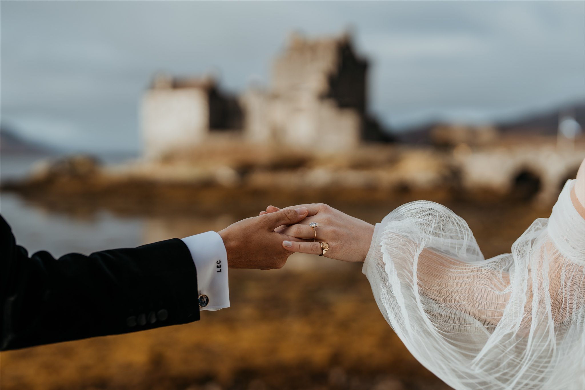 Brides hold hands in front of a castle during their Isle of Skye elopement