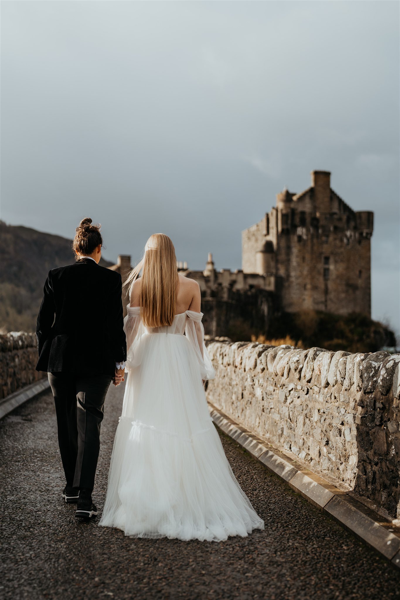 Brides hold hands while walking up to a castle on the Isle of Skye