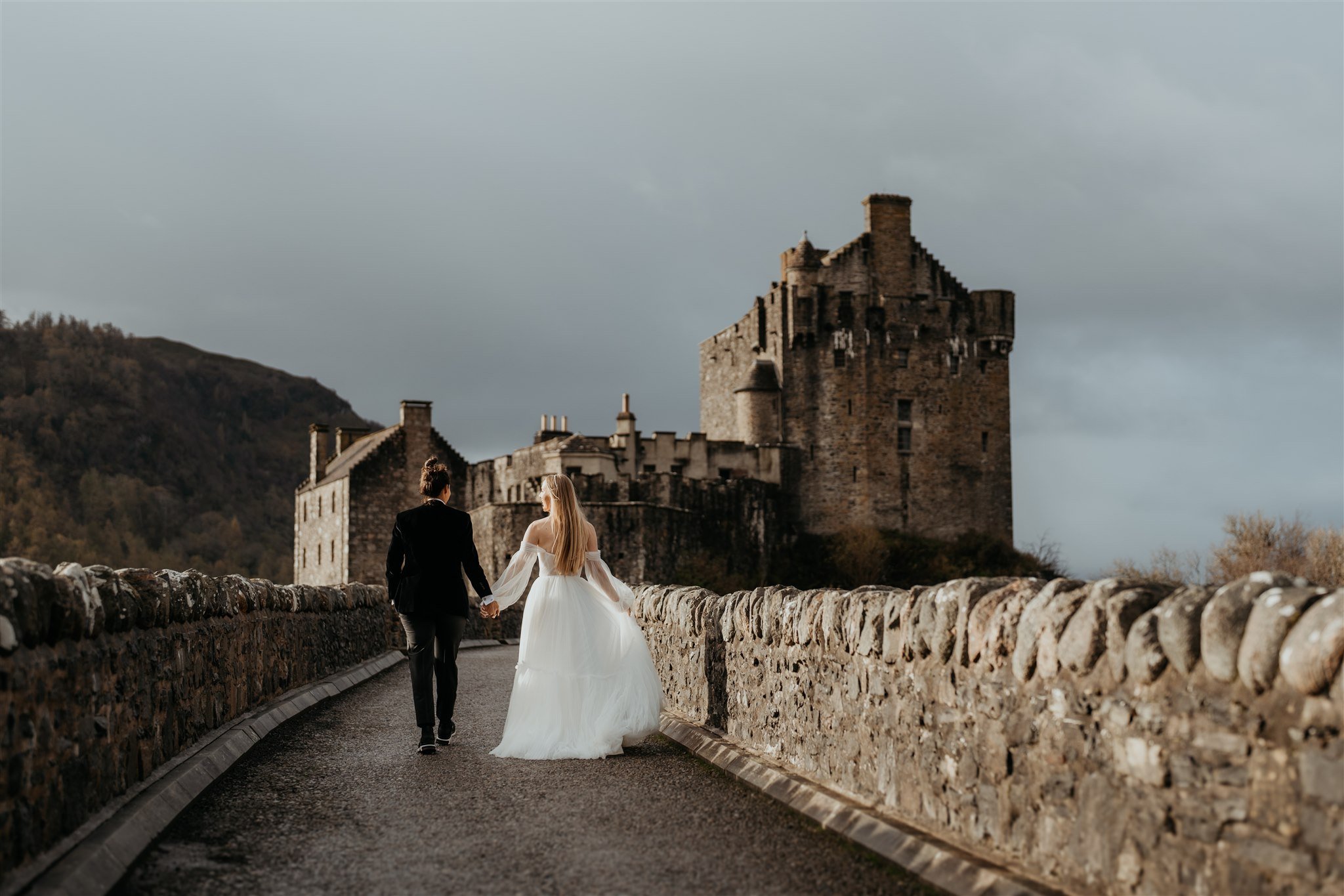 Brides hold hands while walking up to a castle on the Isle of Skye