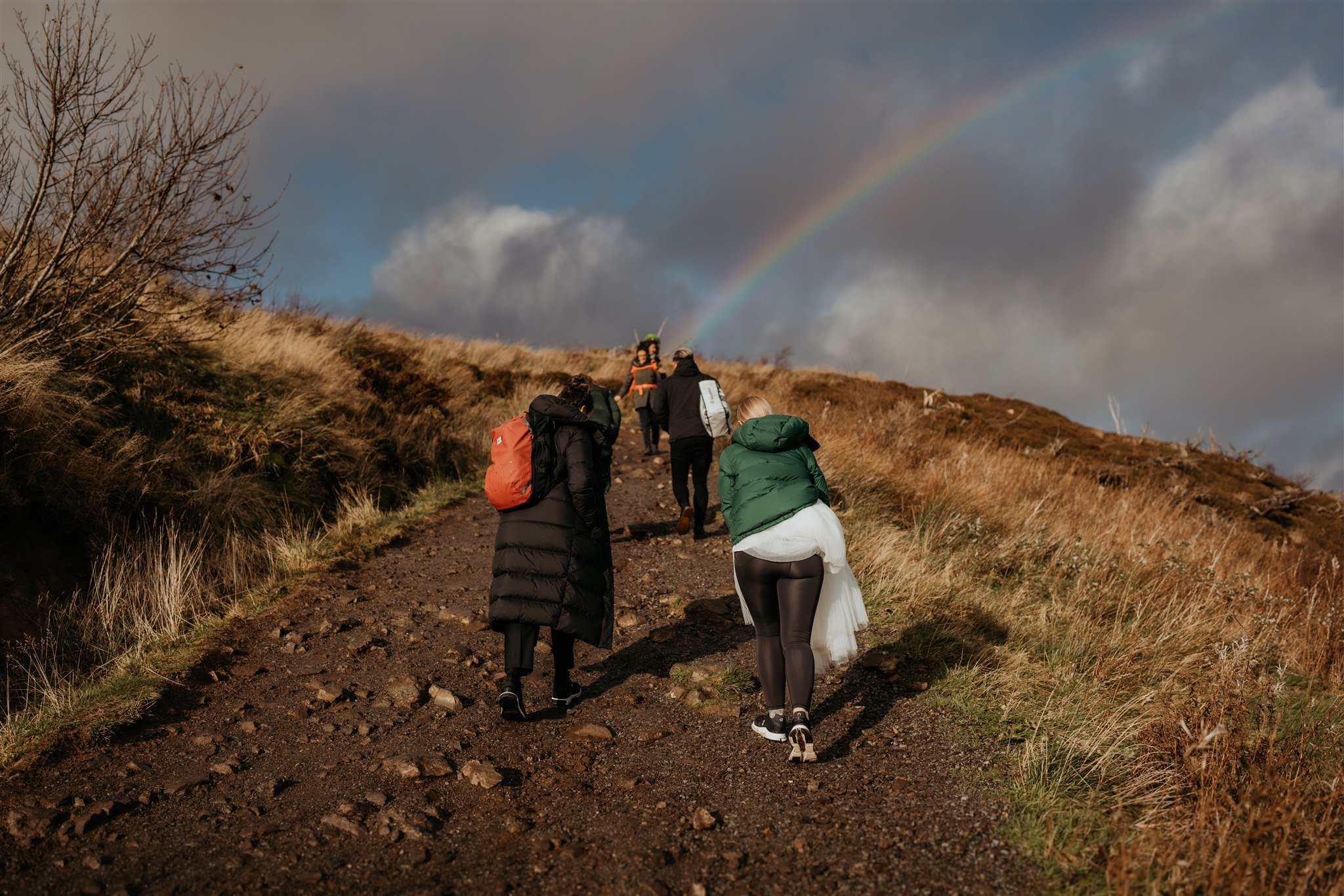 Rainbow in the sky while two brides hike to elopement ceremony location on the Isle of Skye
