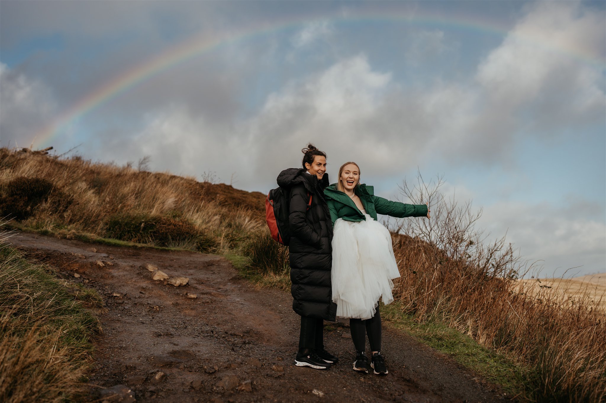 Rainbow in the sky arching over two brides hiking to their elopement ceremony on the Isle of Skye