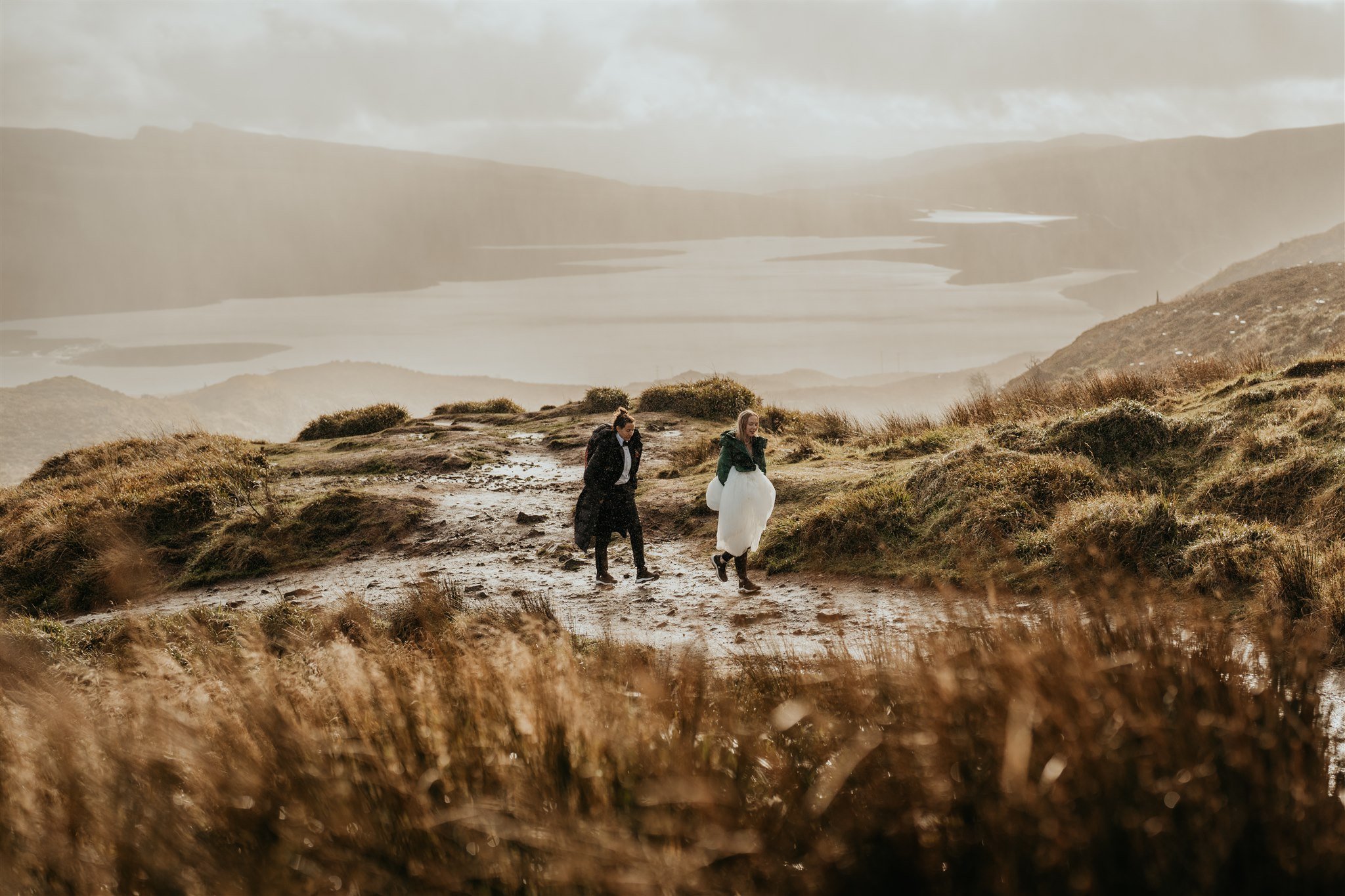 Brides hike through a muddy trail to their Isle of Skye elopement location