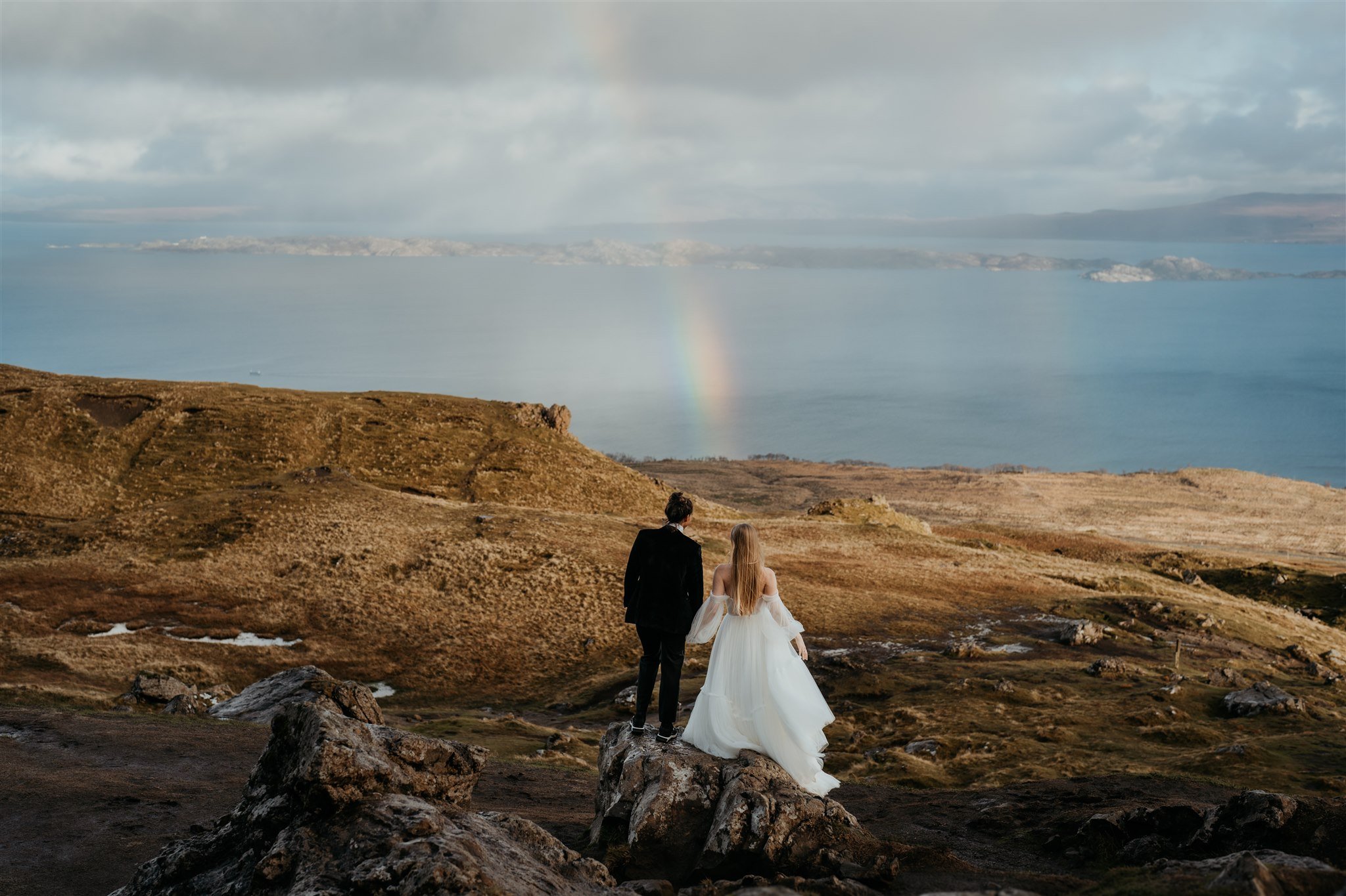 Brides look out at a rainbow in the sky before their Isle of Skye elopement ceremony