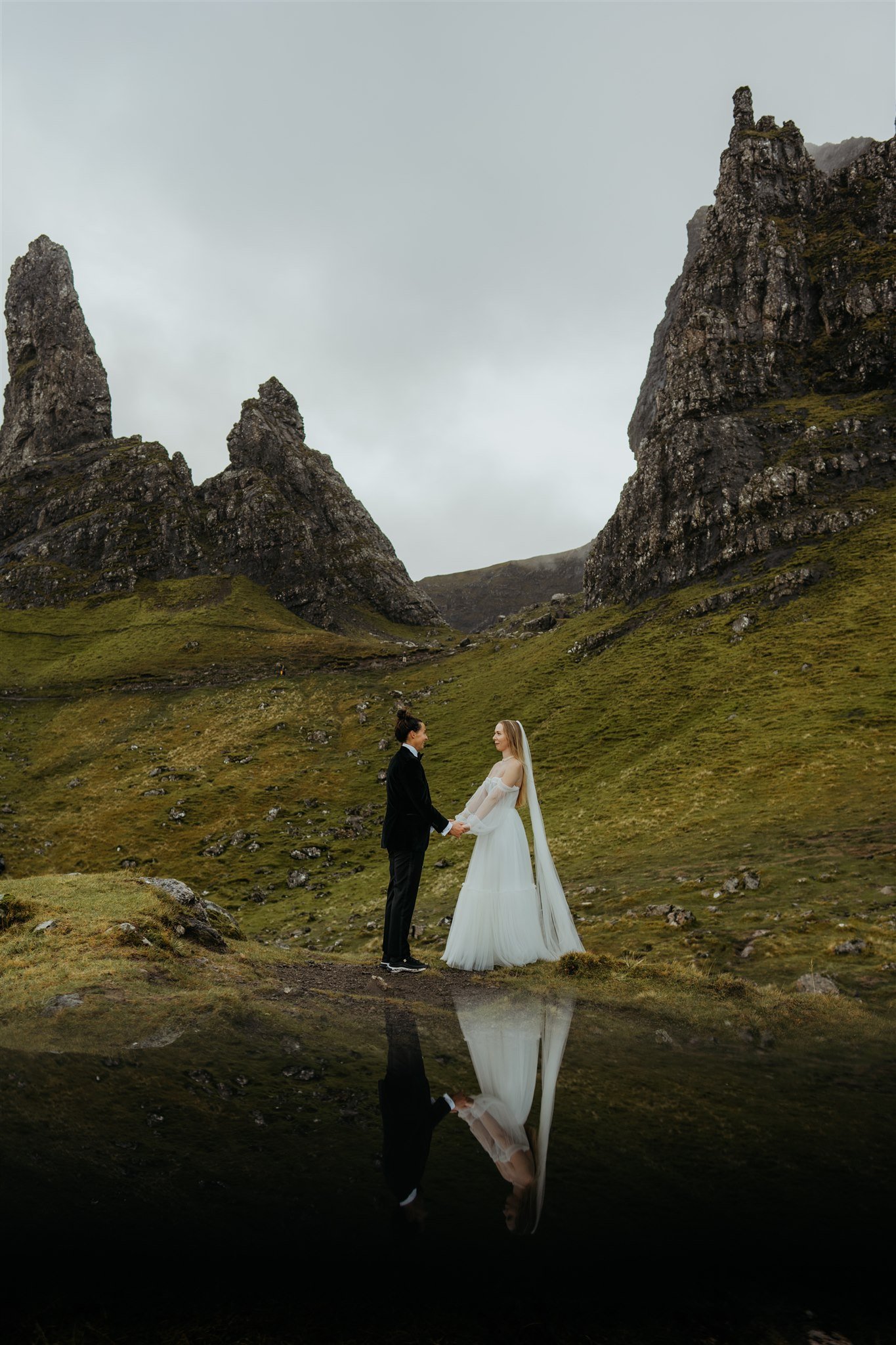 Brides hold hands and exchange vows while standing on a mossy hill during their elopement on the Isle of Skye