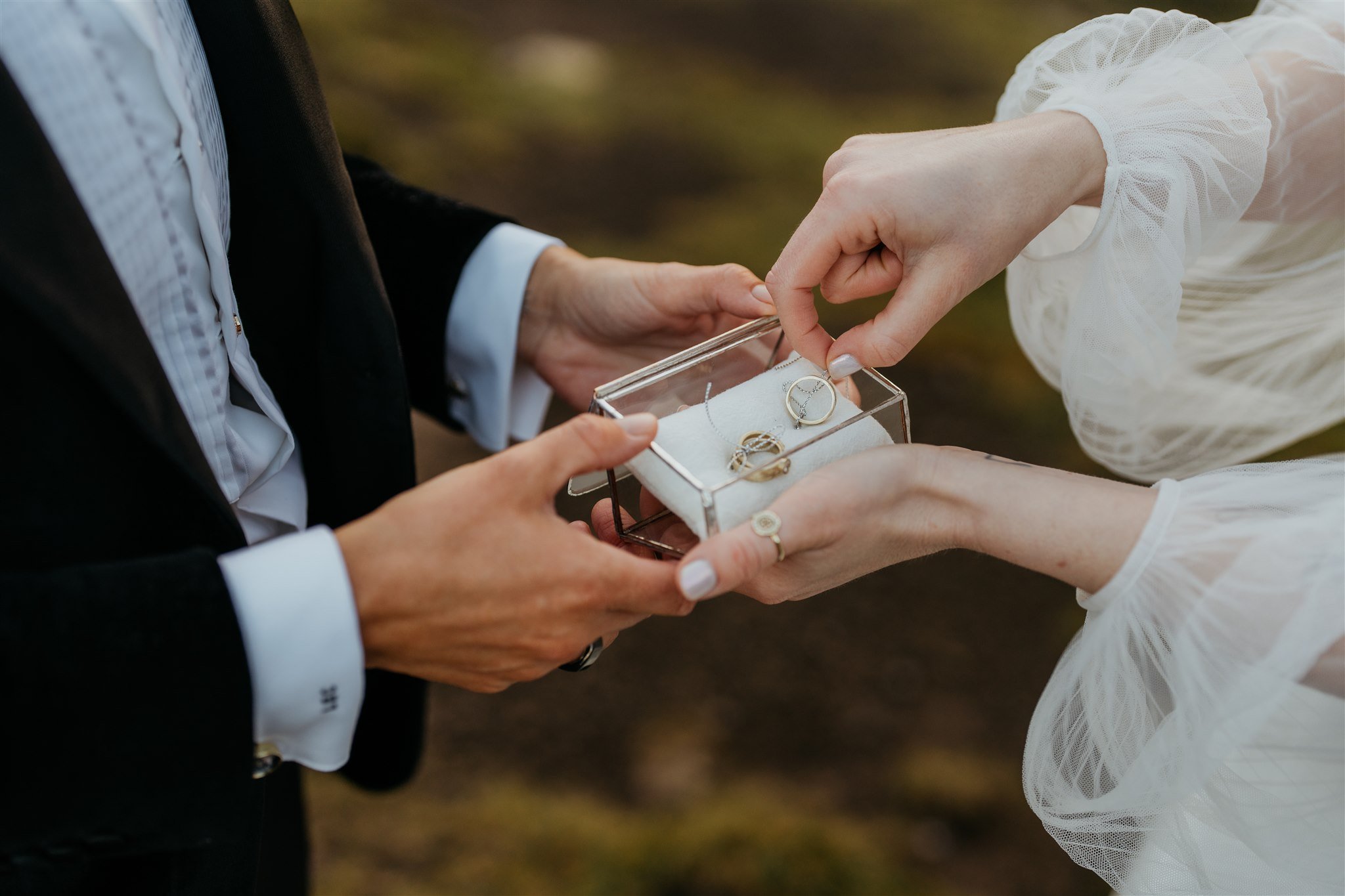 Brides pick up rings from clear ring box during their elopement in Scotland