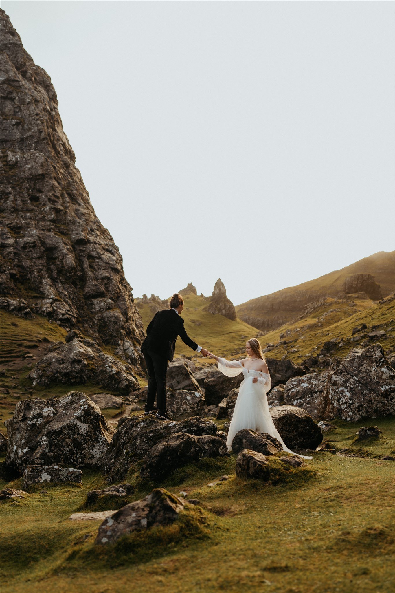 Brides help each other up the hill during their adventure photos at their Isle of Skye elopement