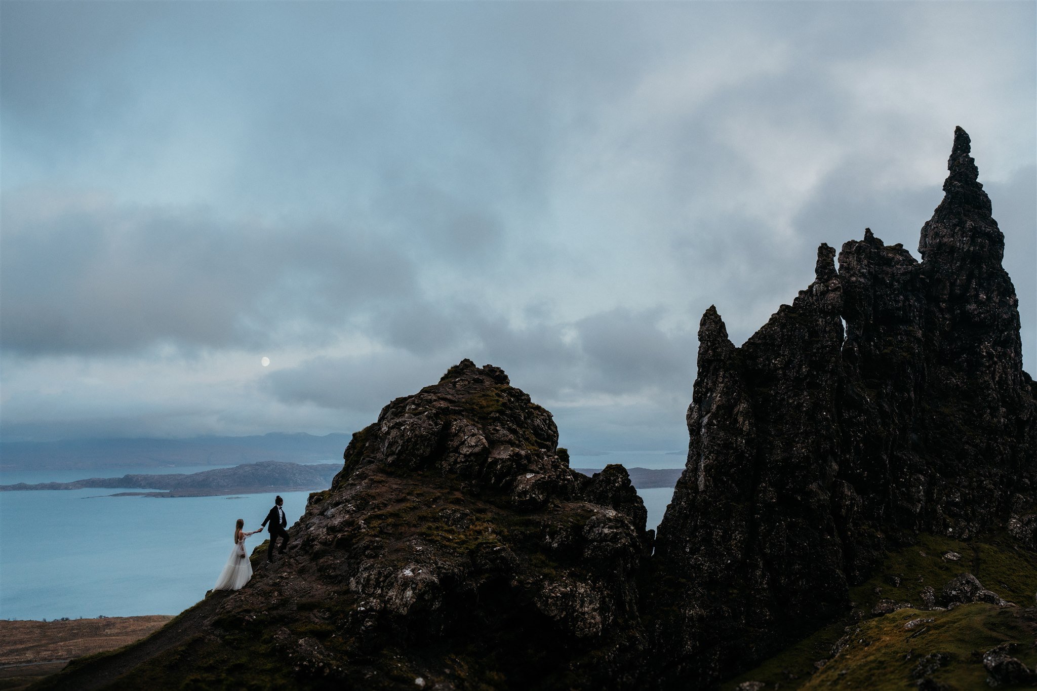 Brides hold hands as they walk up a hill on the Isle of Skye during blue hour