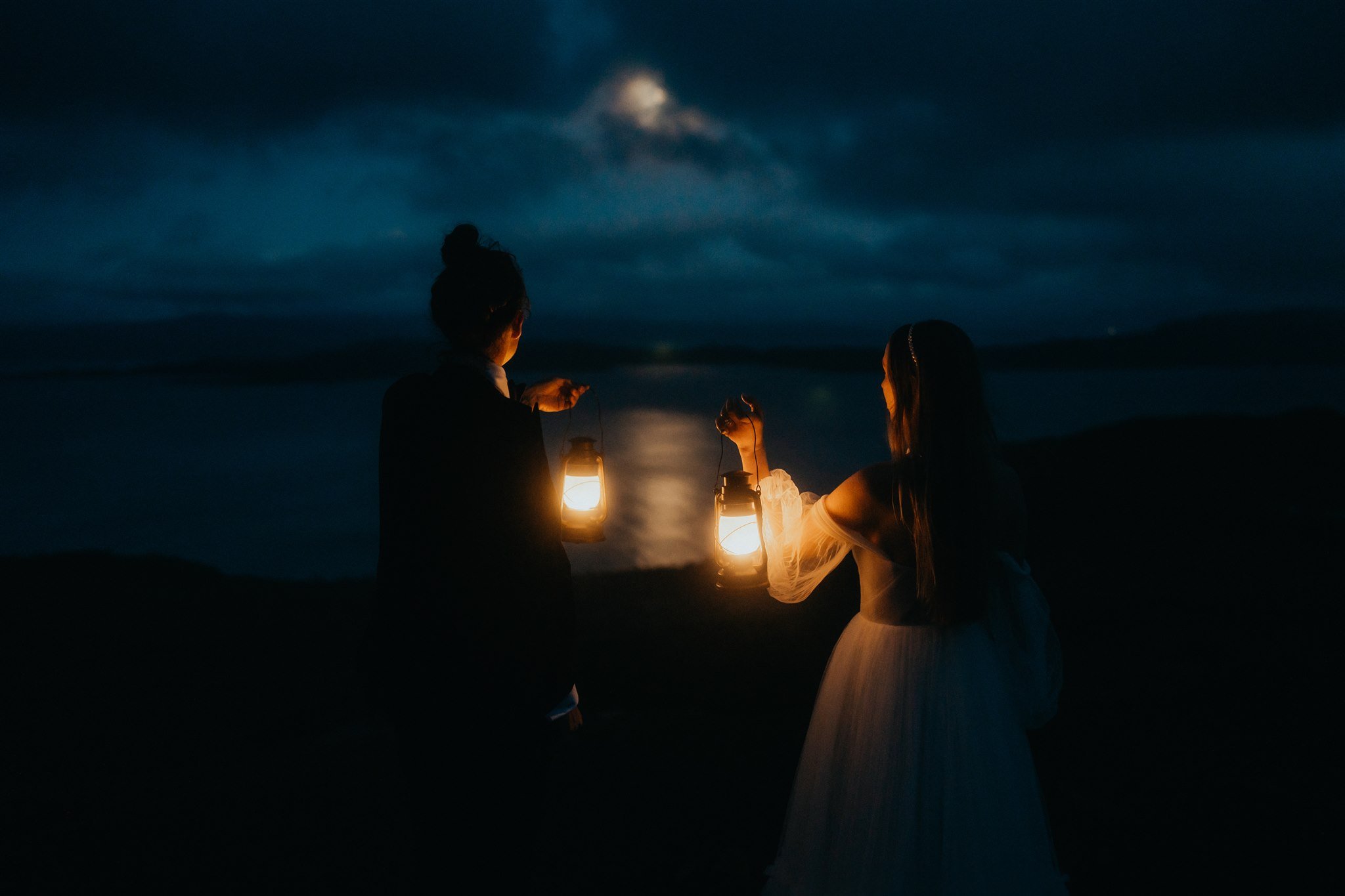 Brides holding lanterns looking out at the moon during their Isle of Skye elopement