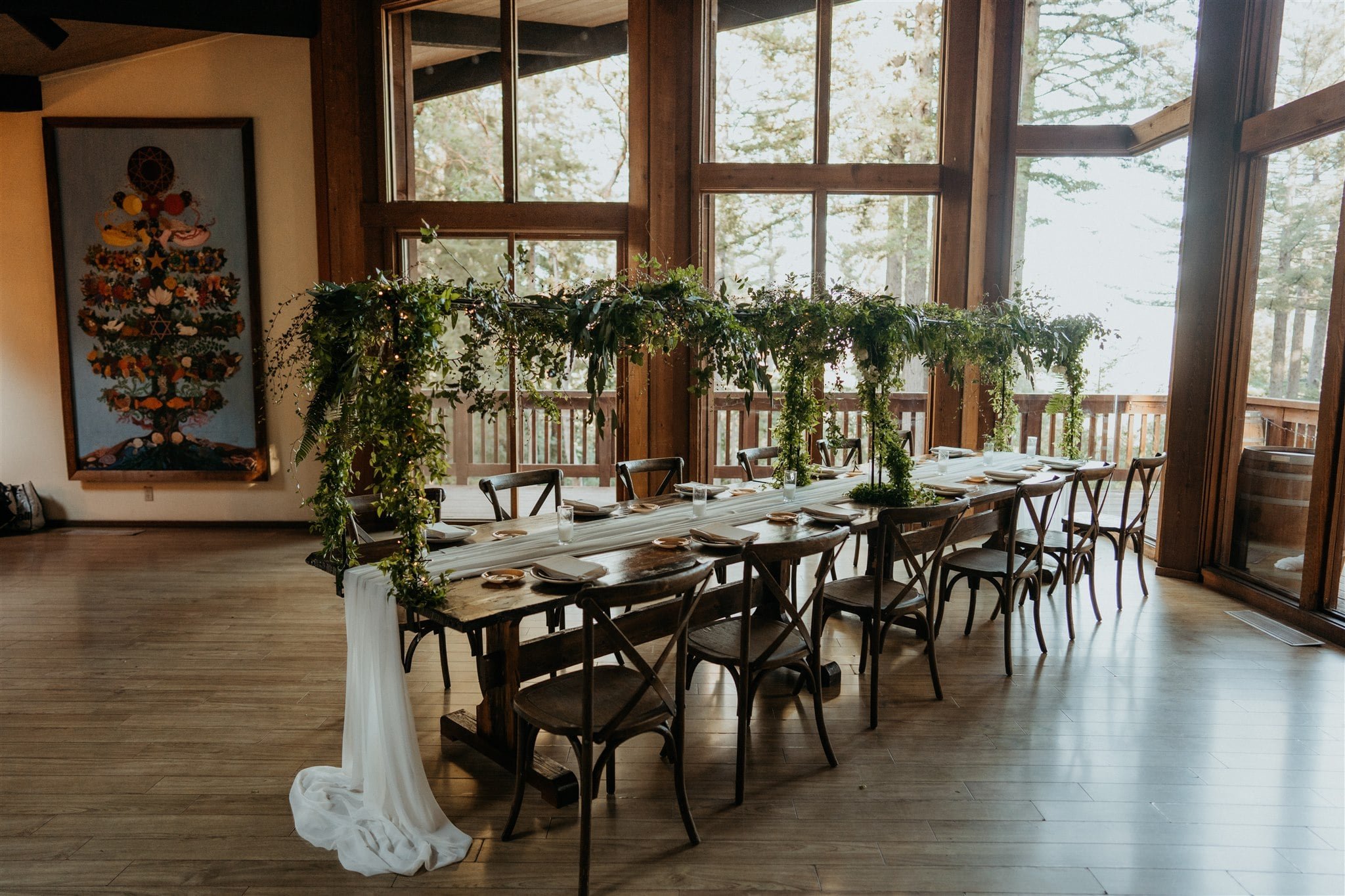 Indoor reception table with greenery arch and white table runner at Sequoia Retreat Center