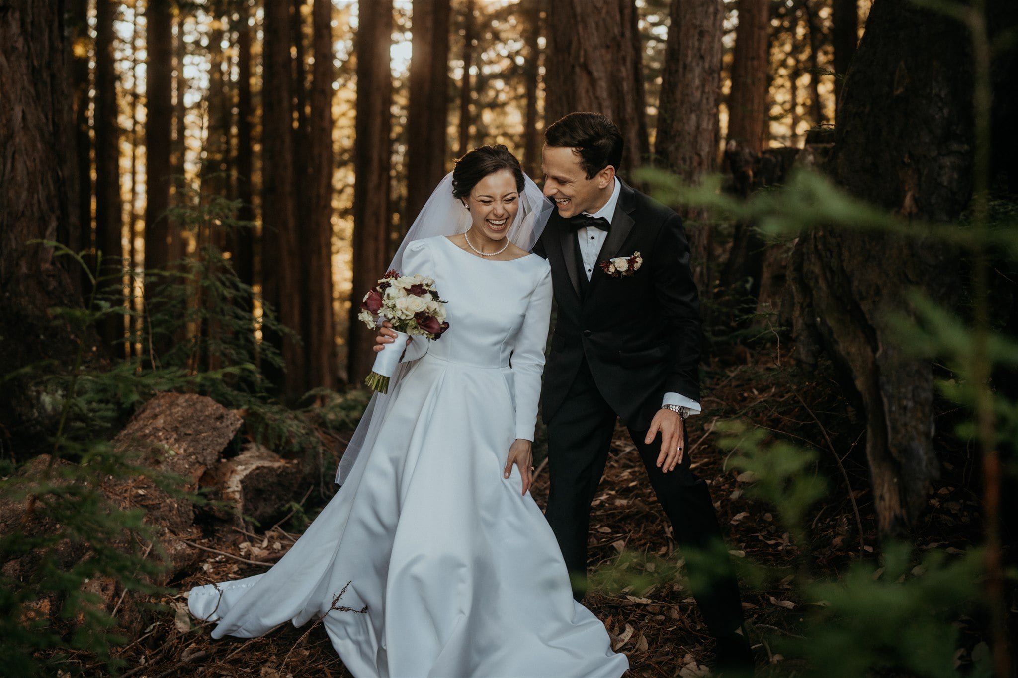 Bride and groom laugh while walking through the forest after their California micro wedding