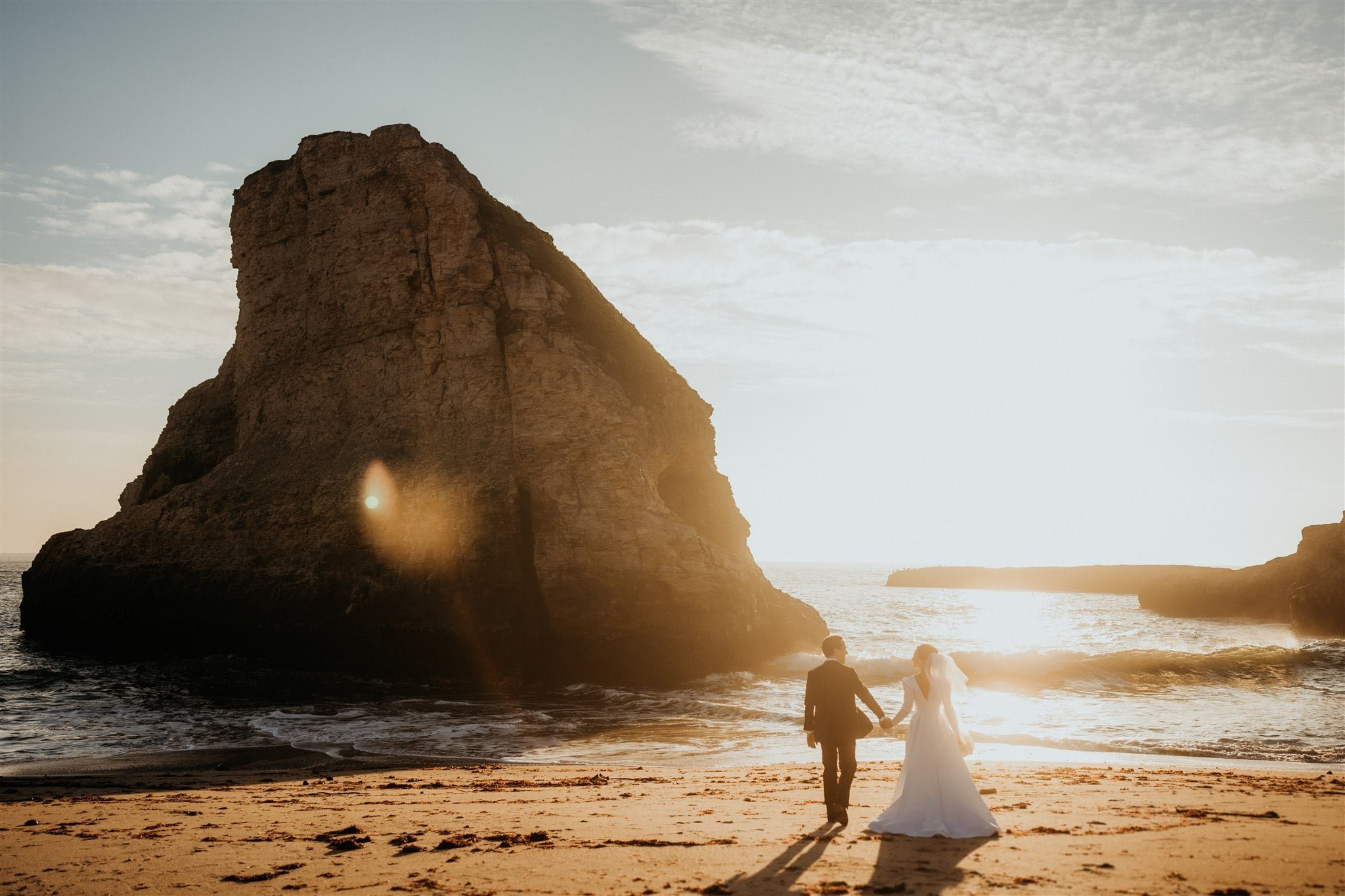 Bride and groom hold hands while walking across the beach after their California micro wedding