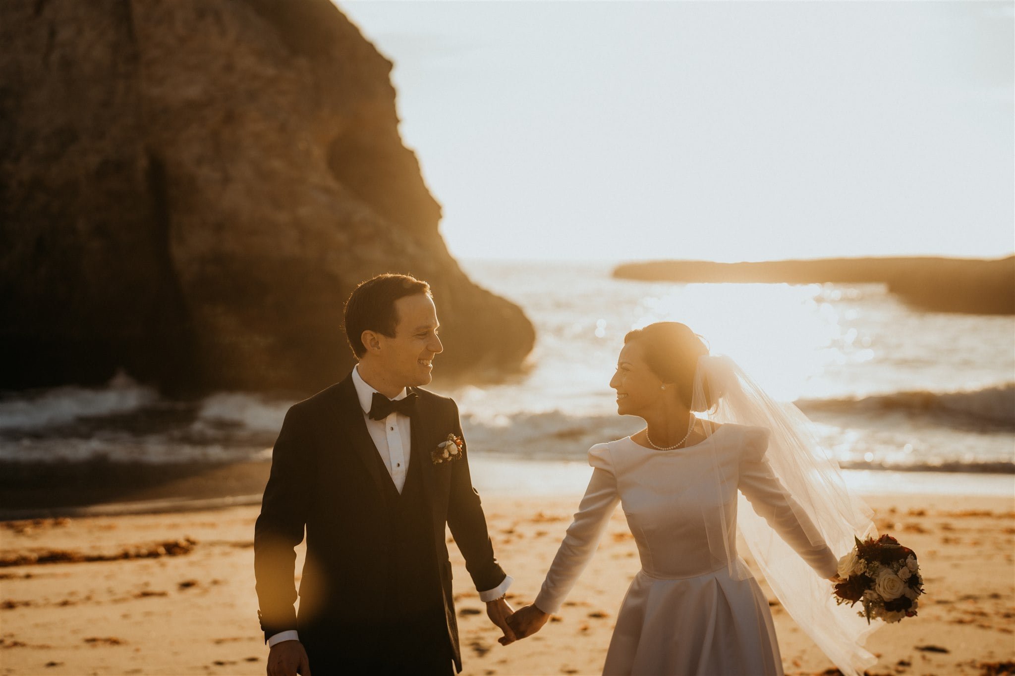 Bride and groom hold hands while walking across the beach after their California micro wedding ceremony