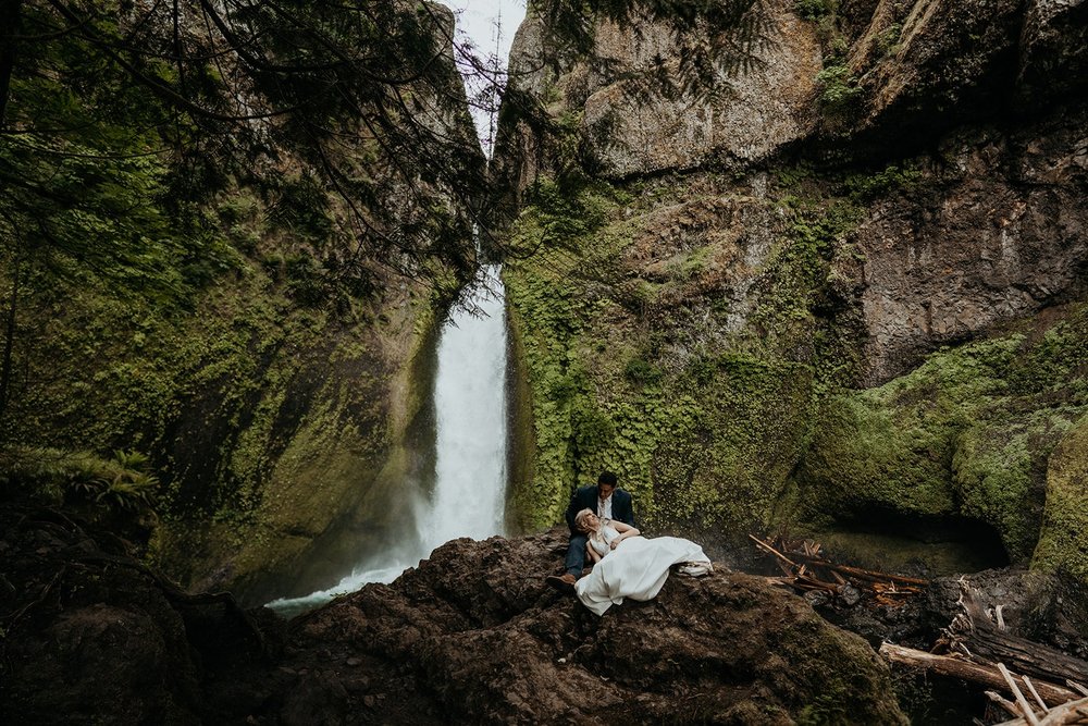 Bride and groom sit in front of a waterfall in the Columbia River Gorge