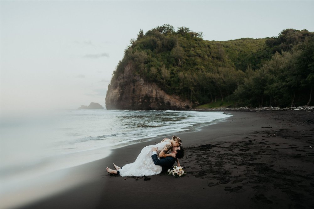 Bride and groom lay on the black sand beach during their elopement on the Big Island