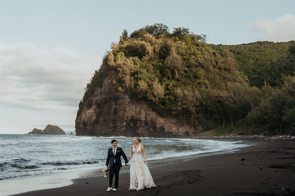 Bride and groom hold hands while walking across the black sand beach during their Big Island elopement